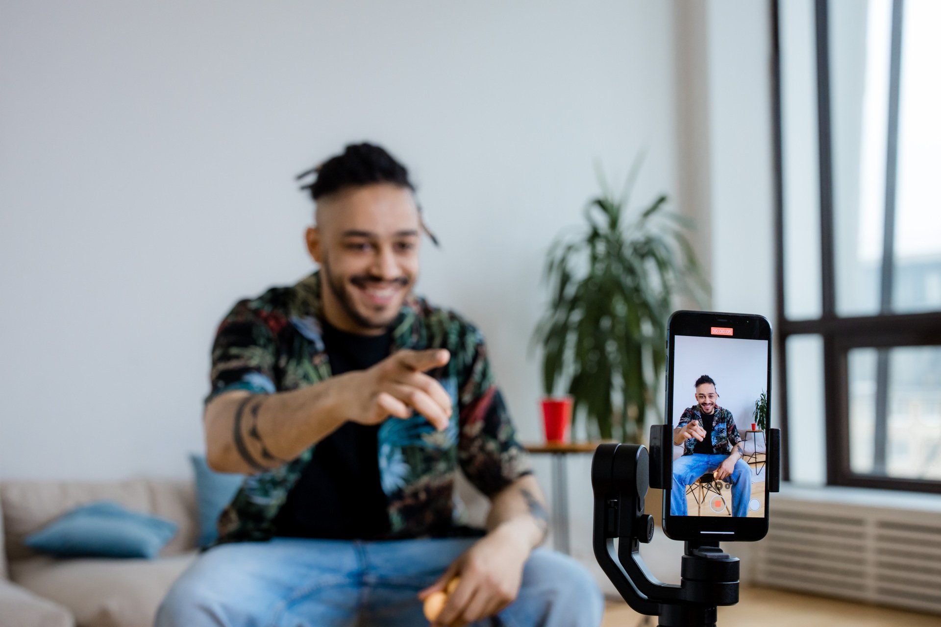 A man is sitting on a couch taking a picture of himself with a cell phone.