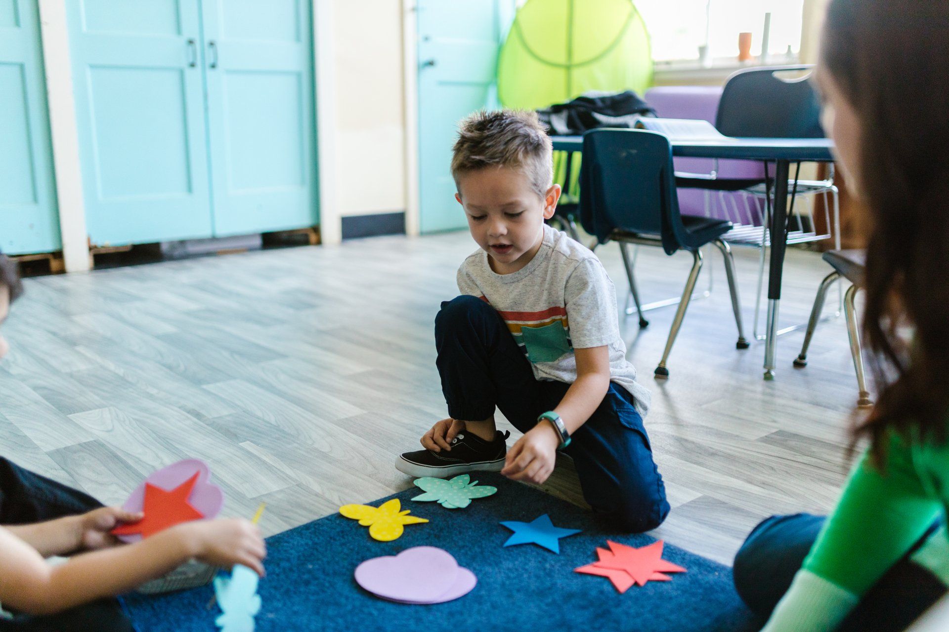 A young boy is sitting on the floor playing with a teacher.