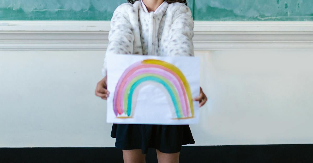 A young girl is holding a drawing of a rainbow.