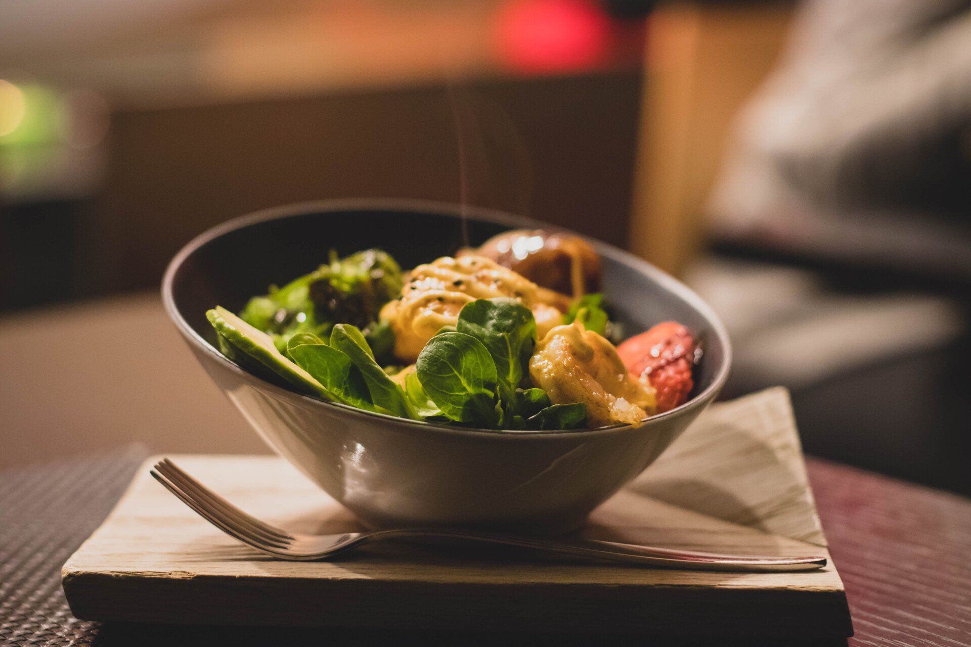 Un bol de salade avec une fourchette sur une planche à découper en bois sur une table.
