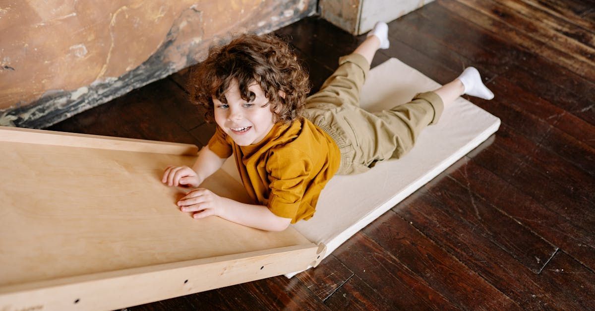 Happy curly-haired child lying on mattress smiling on hardwood floor