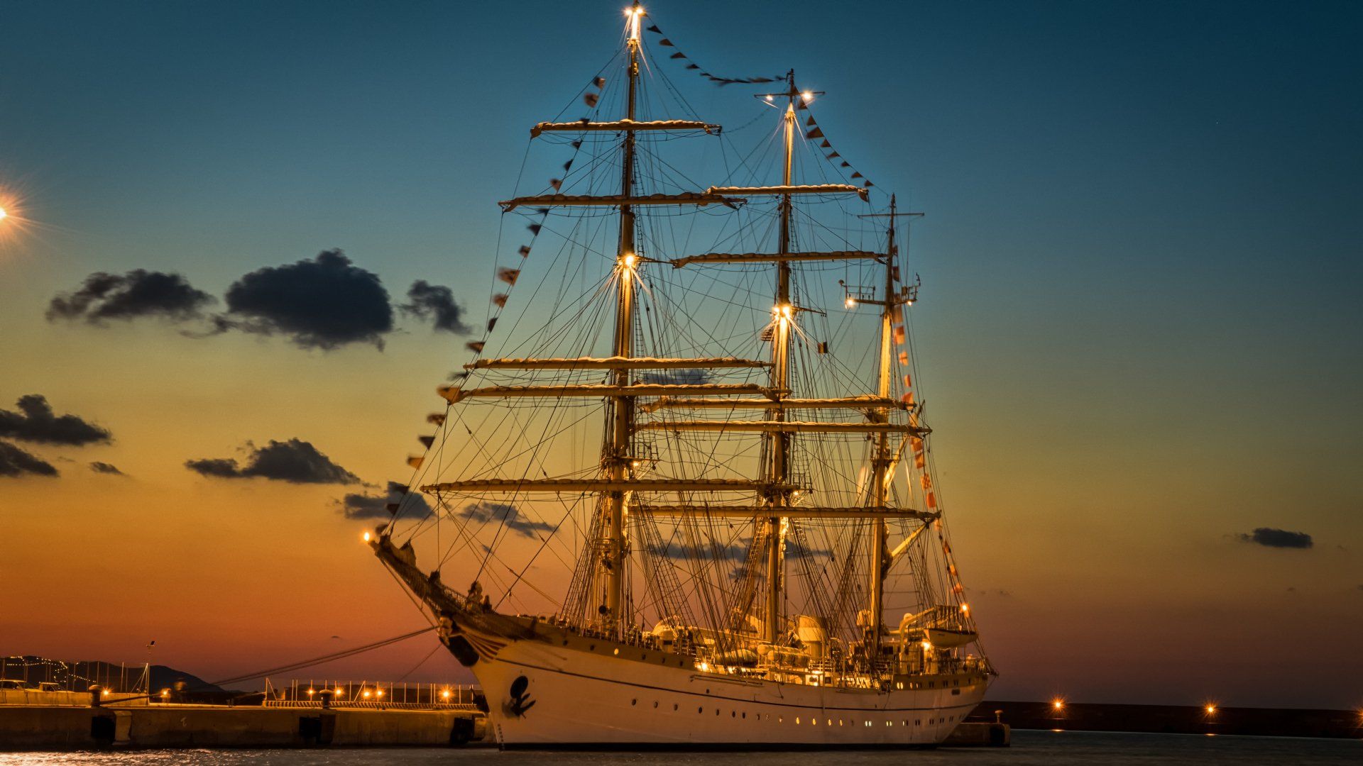 A large sailboat is docked in a harbor at sunset.