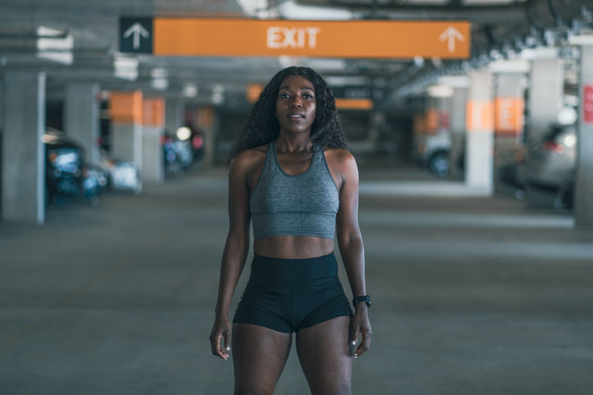 Woman in athletic wear stands in parking garage, looking forward;