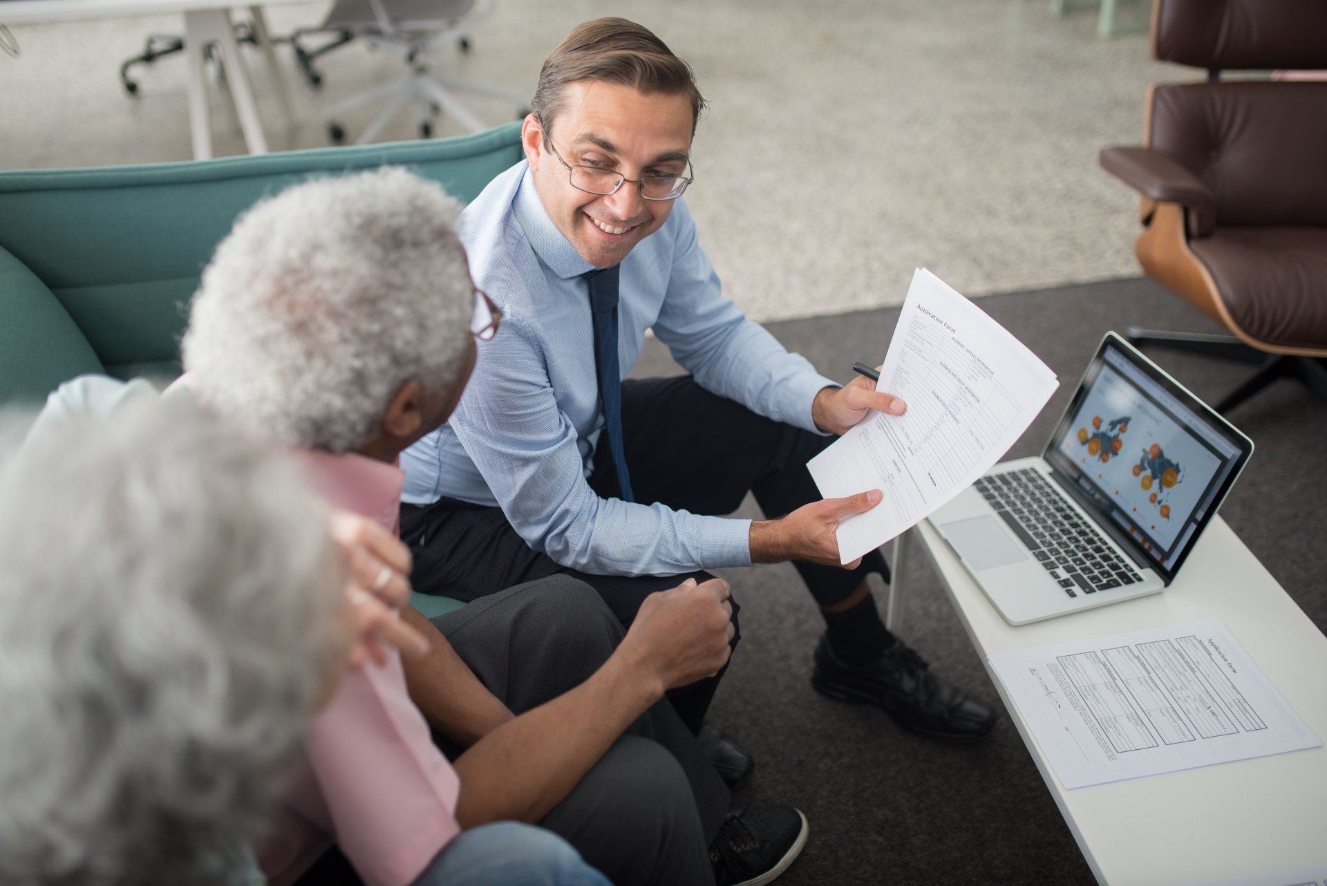 A man is sitting on a couch talking to two elderly people.