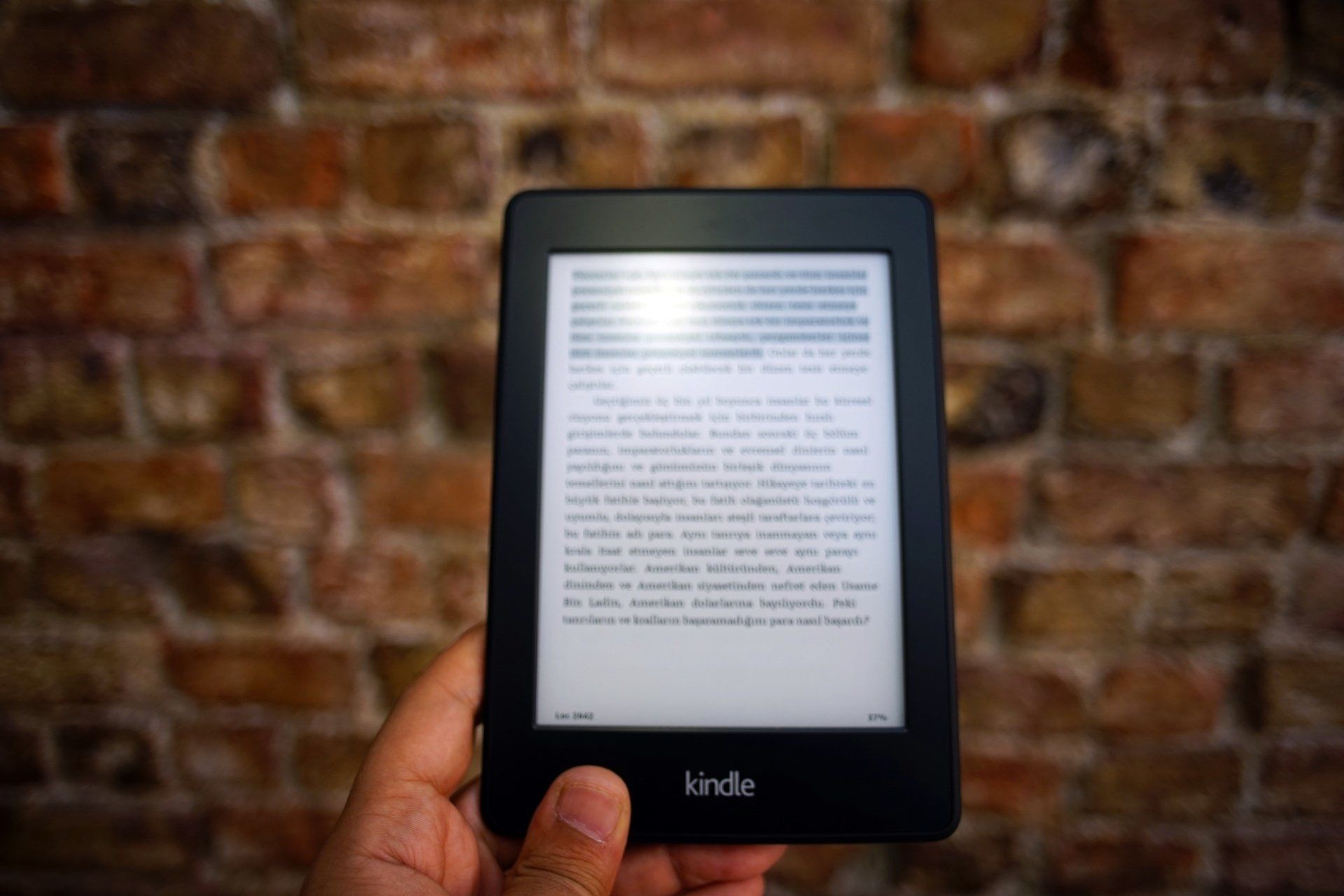 Kindle Unlimited (KU) A person holding a Kindle e-reader in front of a brick wall, displaying text on its screen.
