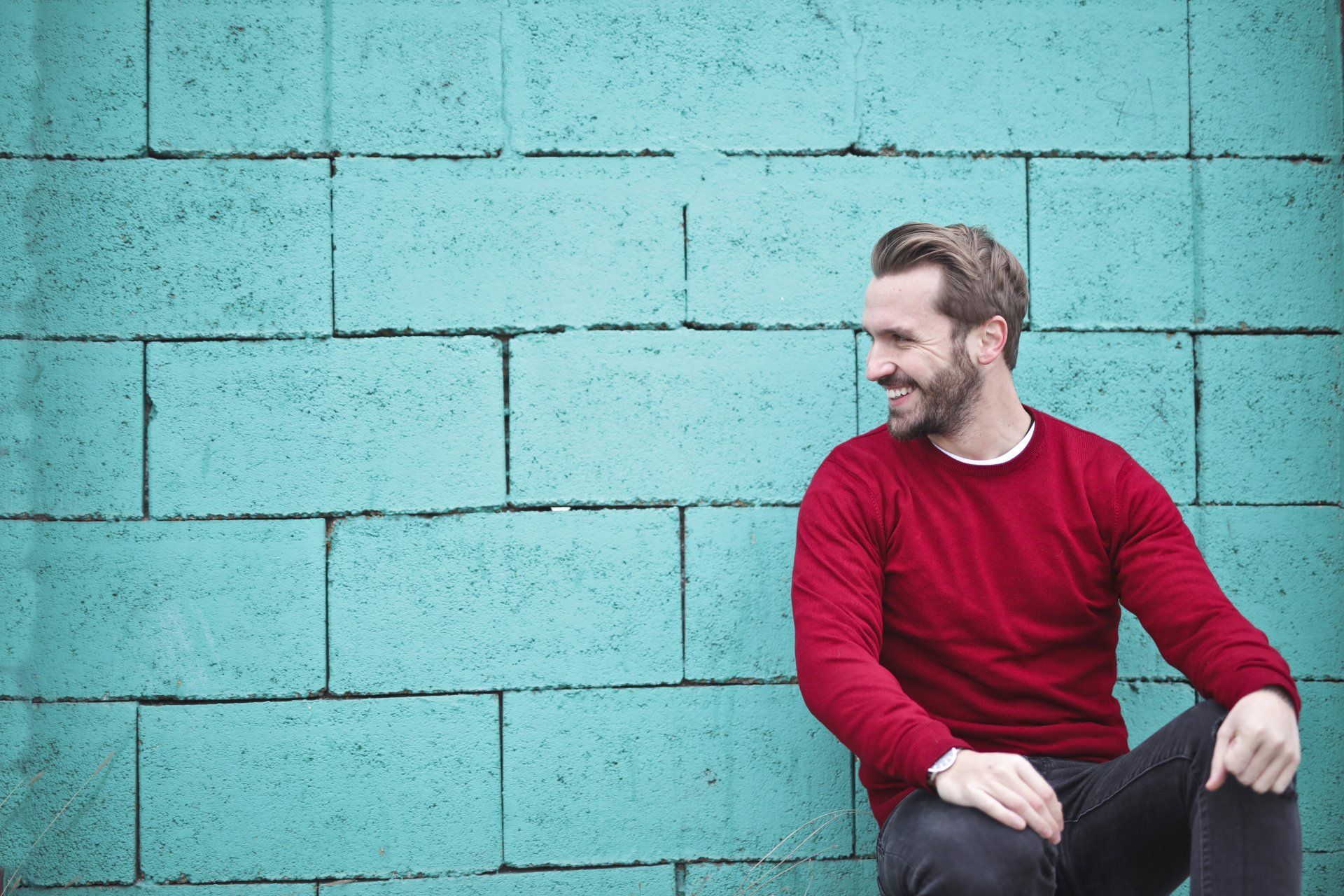 A man sitting up against a concrete block wall, painted turquoise
