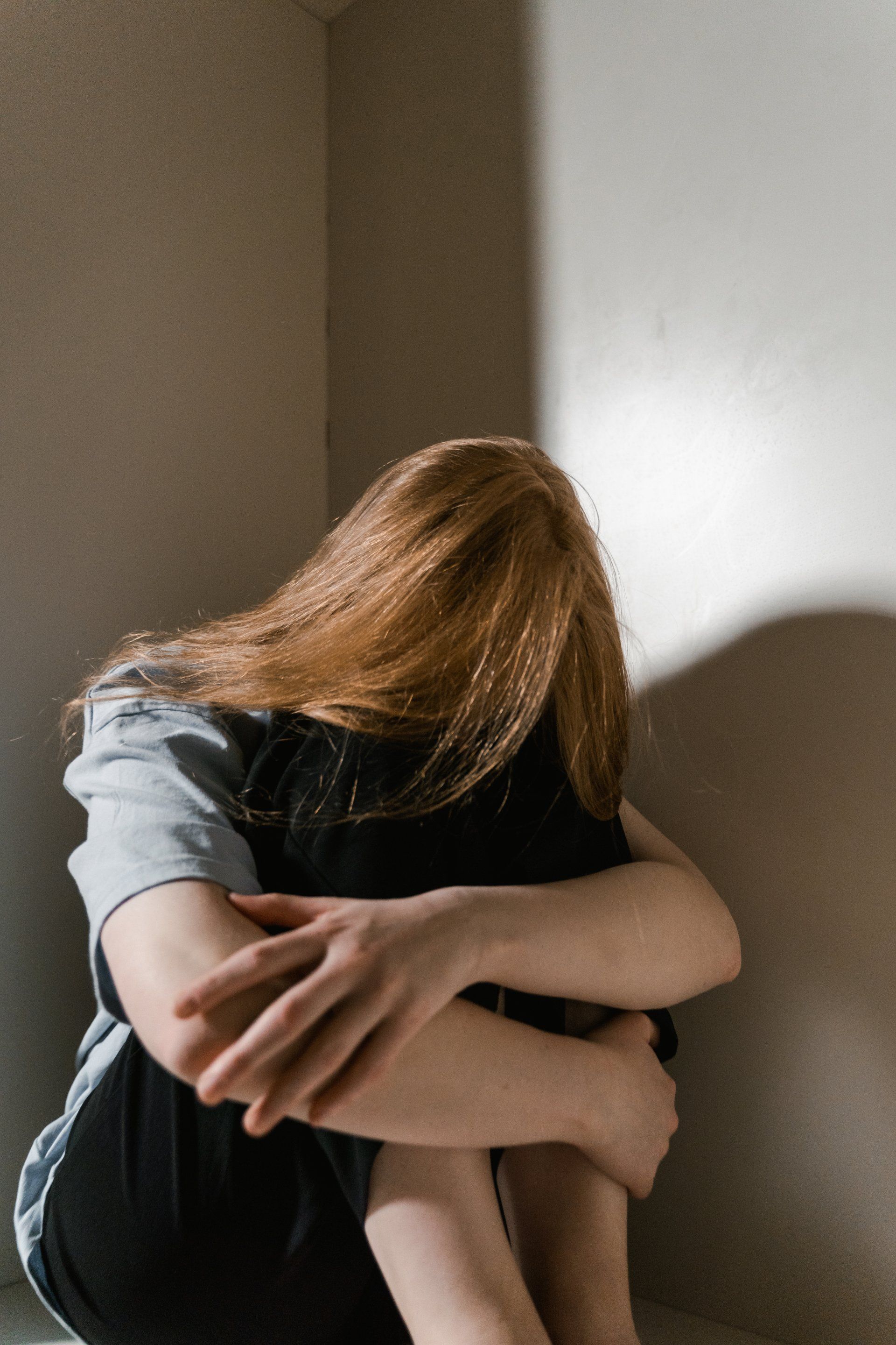 Une femme est assise dans un coin avec sa tête dans ses mains.