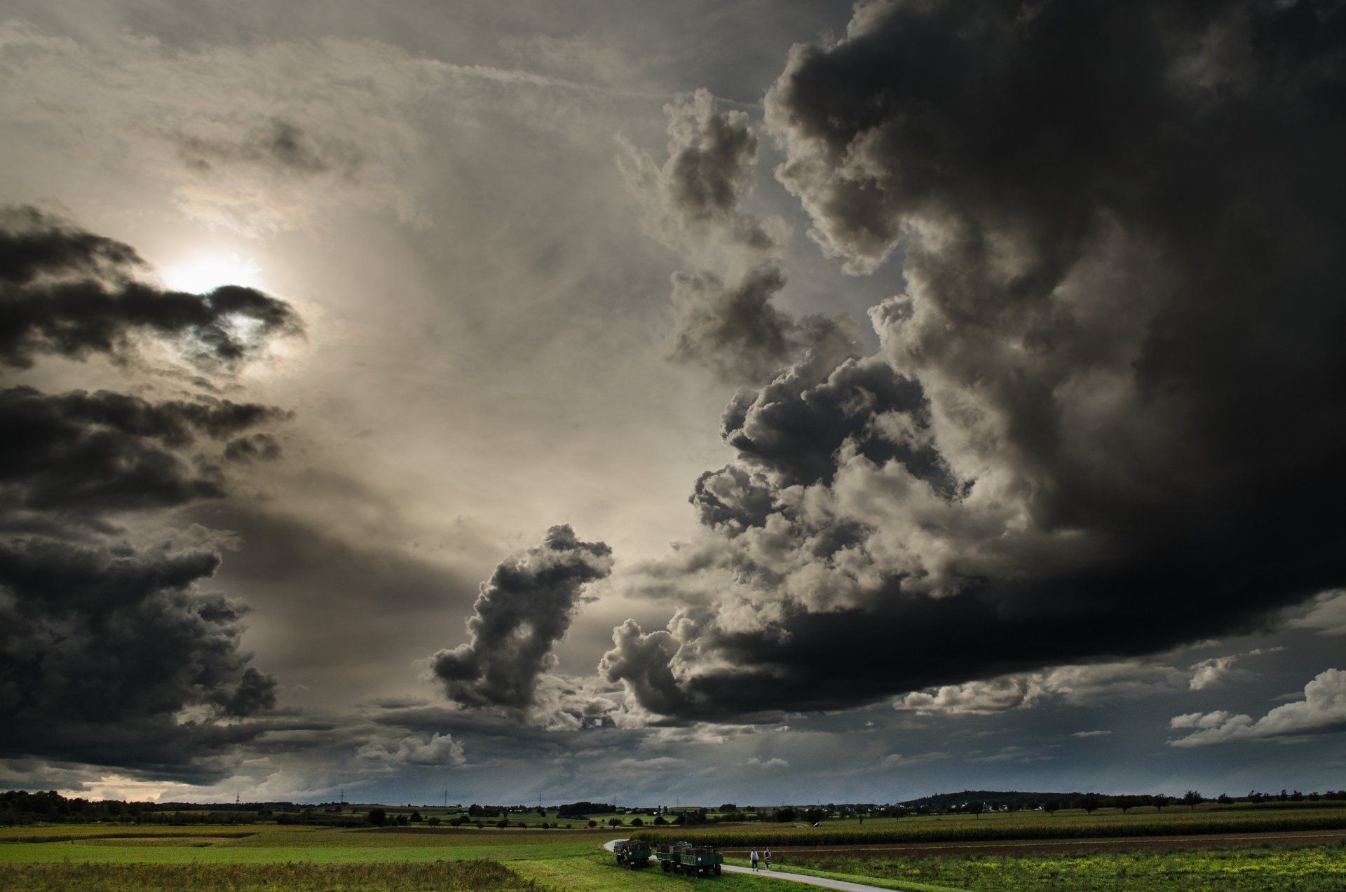 A tractor is driving through a field with a cloudy sky in the background.