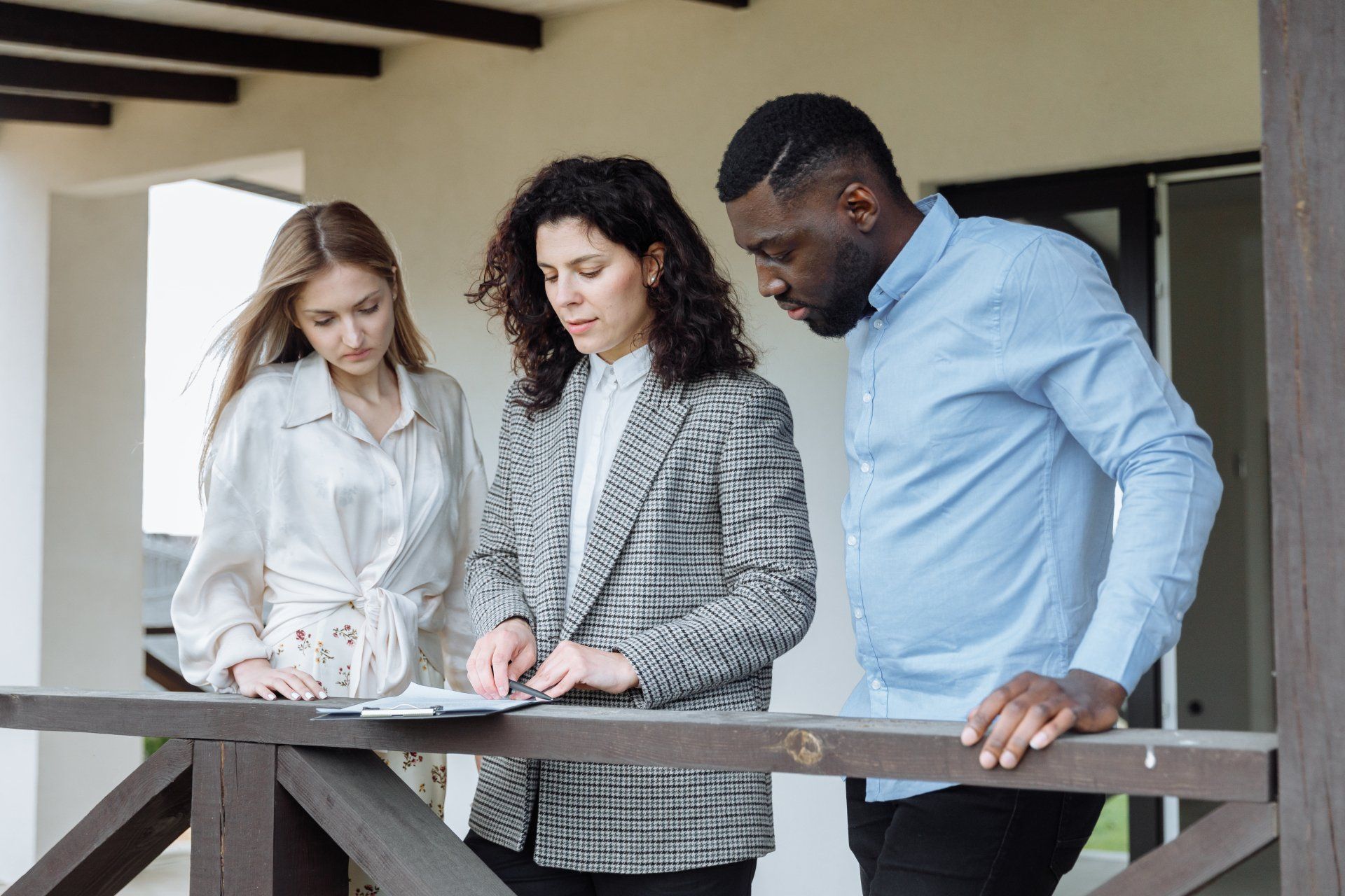 A man and two women are standing on a balcony looking at a blueprint.