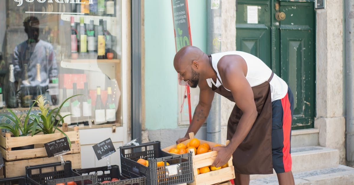 a man in an apron picks oranges from a crate