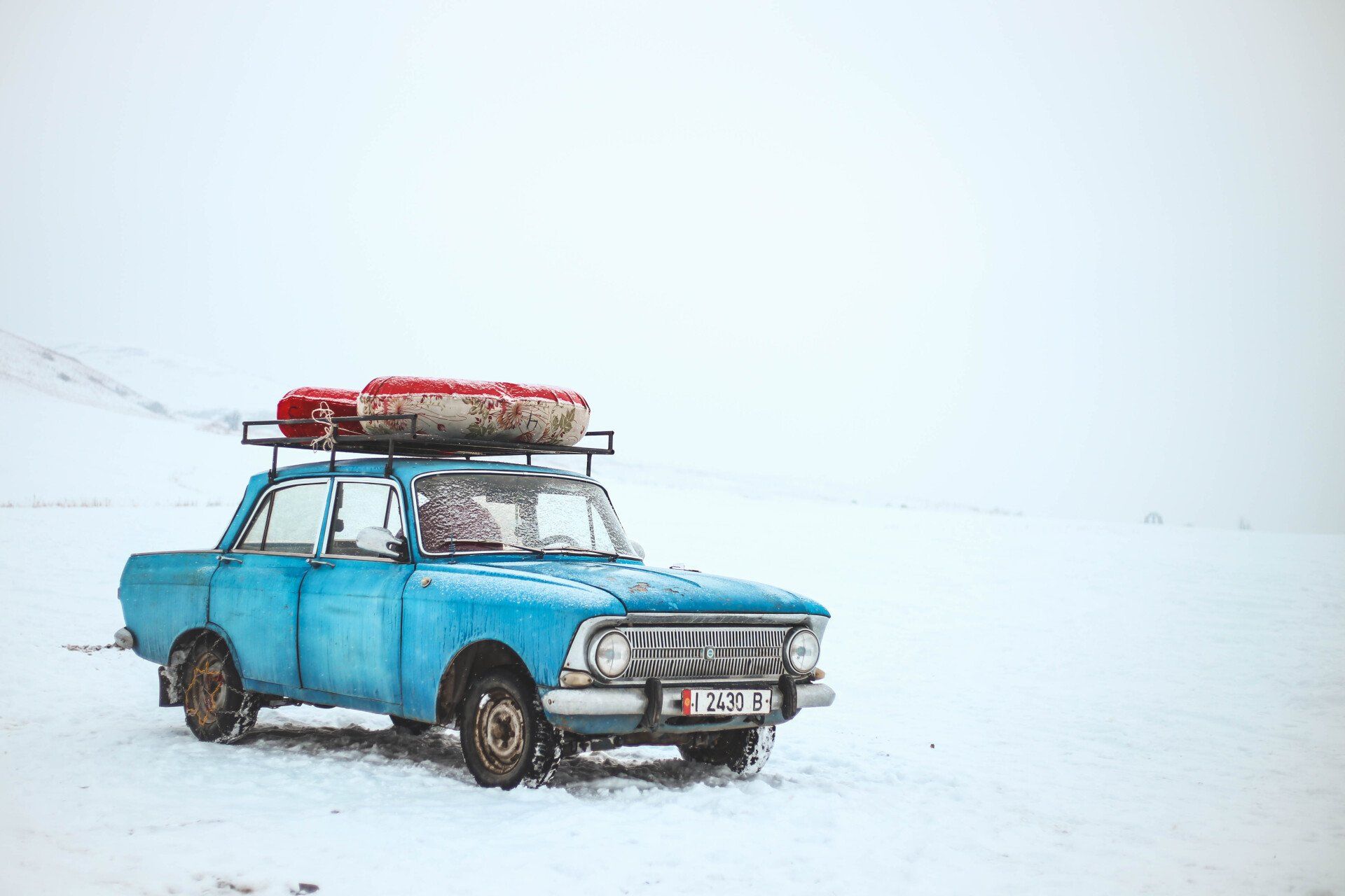 A blue car with luggage on the roof is parked in the snow.
