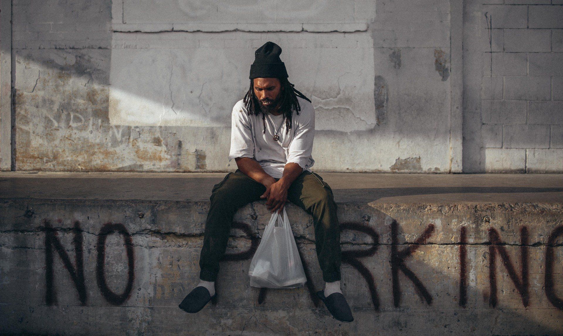 Man with dreadlocks sits, head down, on a concrete ledge marked 