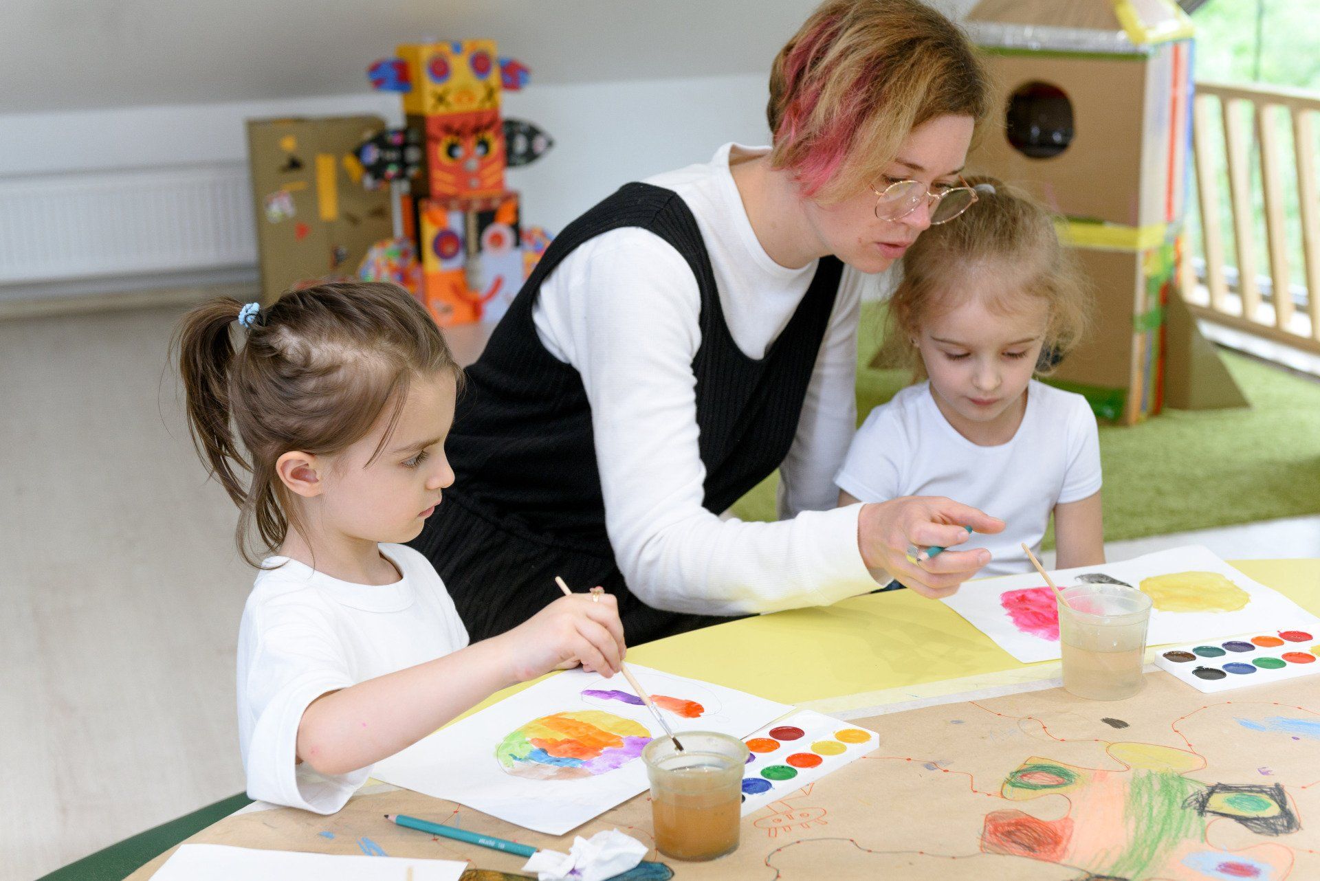 A woman is teaching two little girls how to paint.