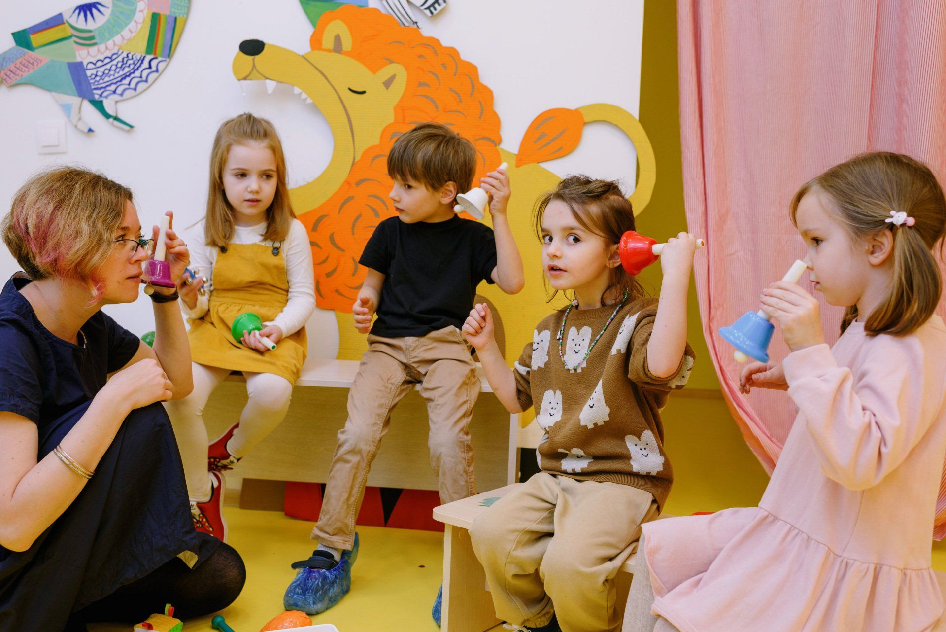 A teacher and four children playing with colorful instruments in a brightly decorated room.