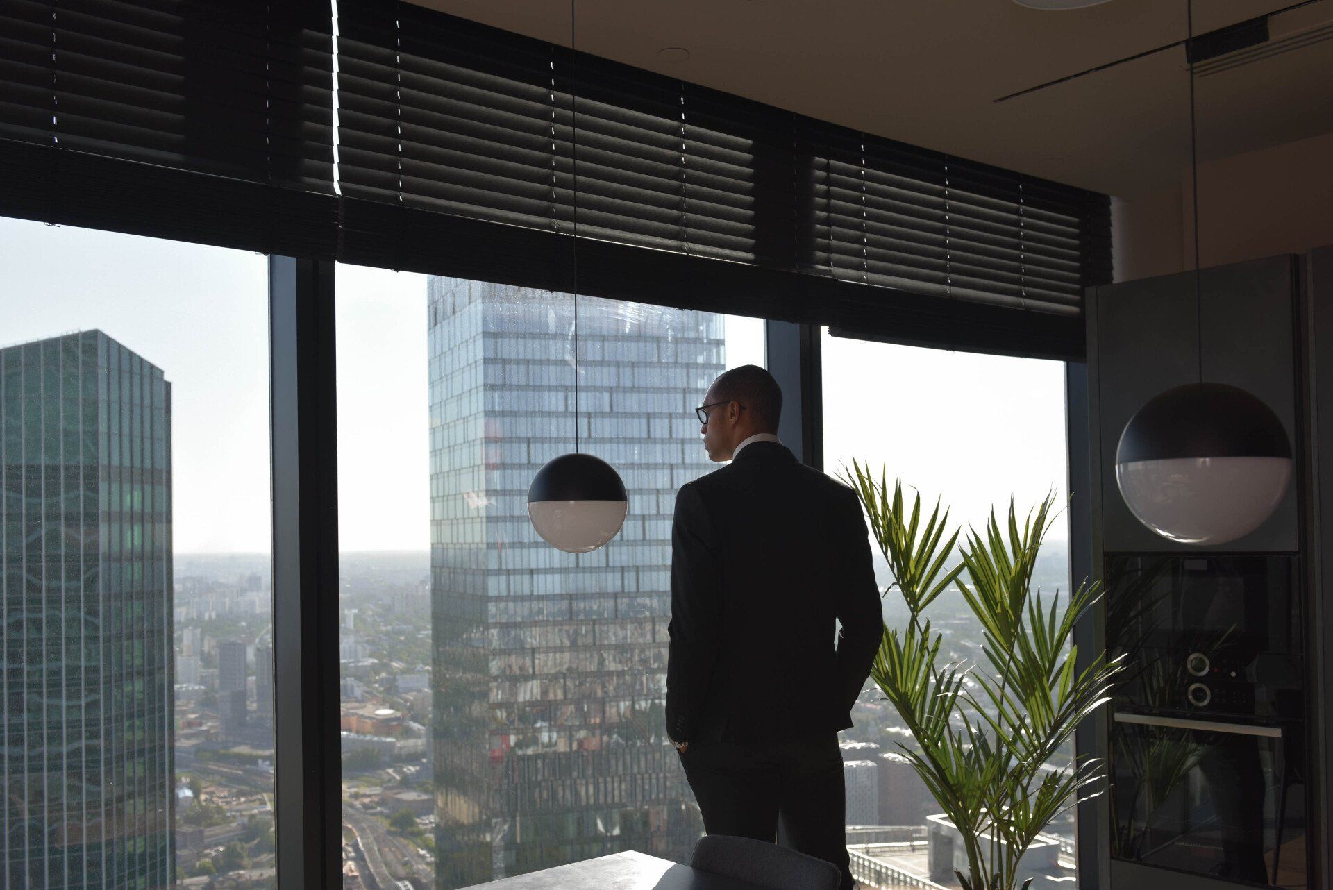 A man in a suit is looking out a window at a city