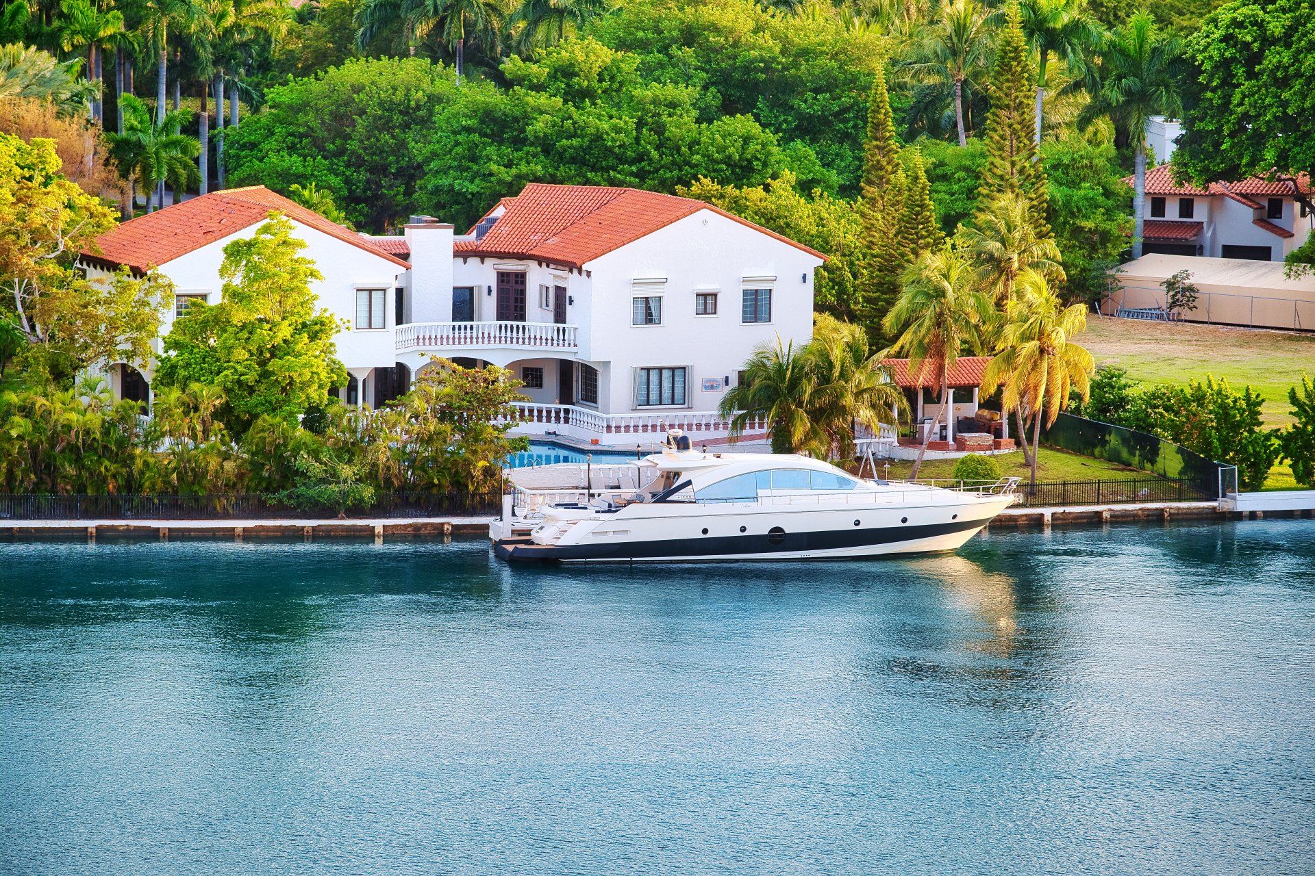 A boat is docked in front of a large house in the water.