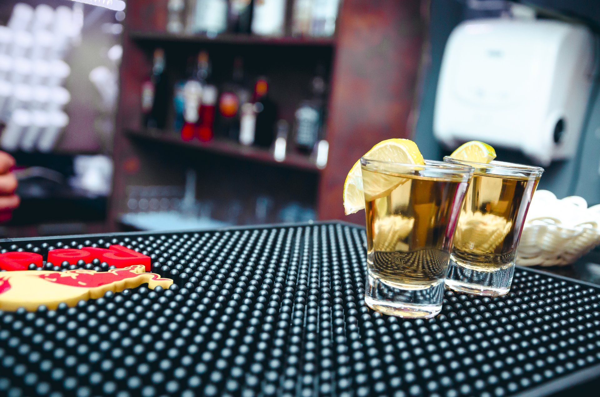 Two shot glasses of tequila with lemon slices on a bar counter.