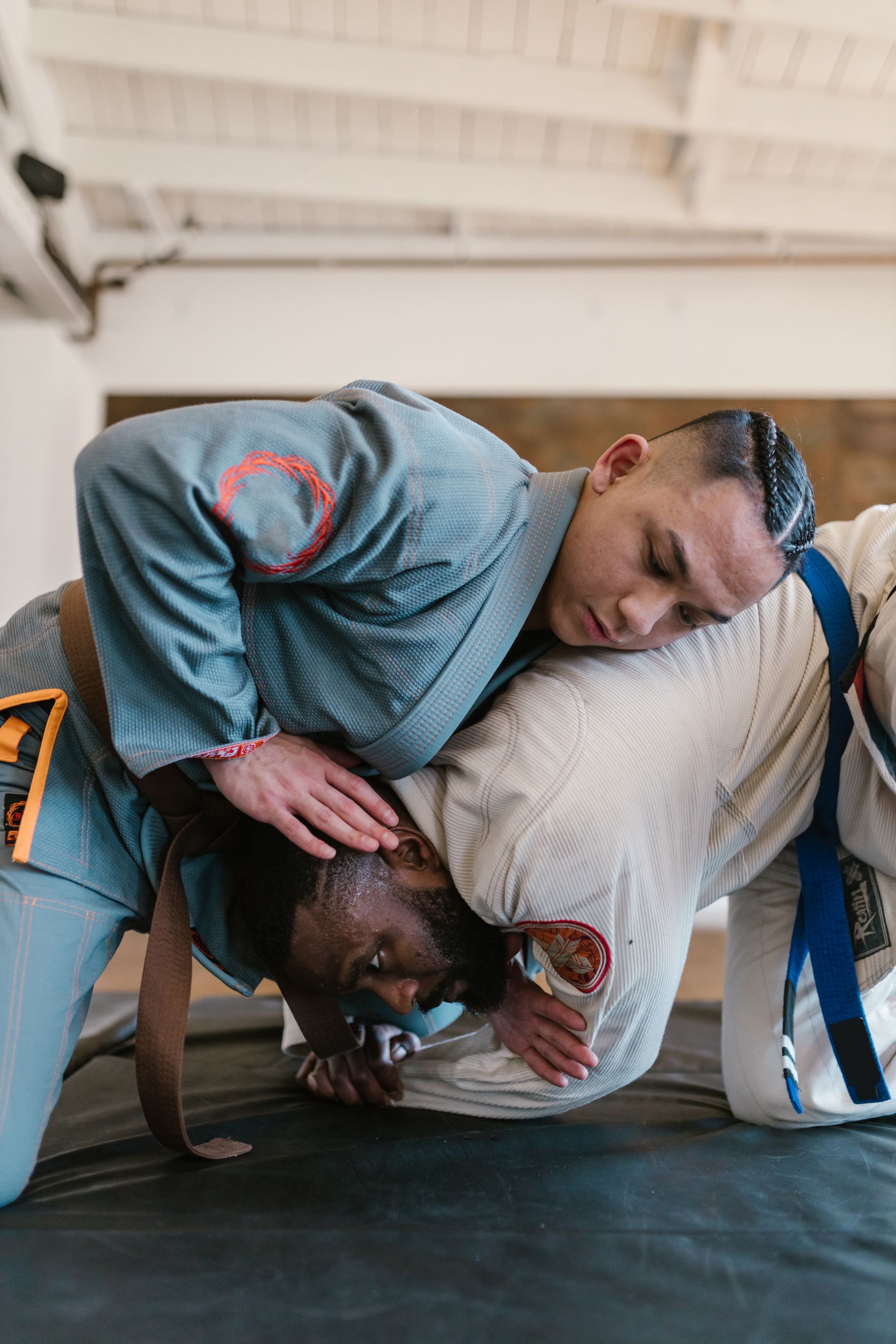 Two people in blue and white gis grappling on a mat; one has the other in a headlock.