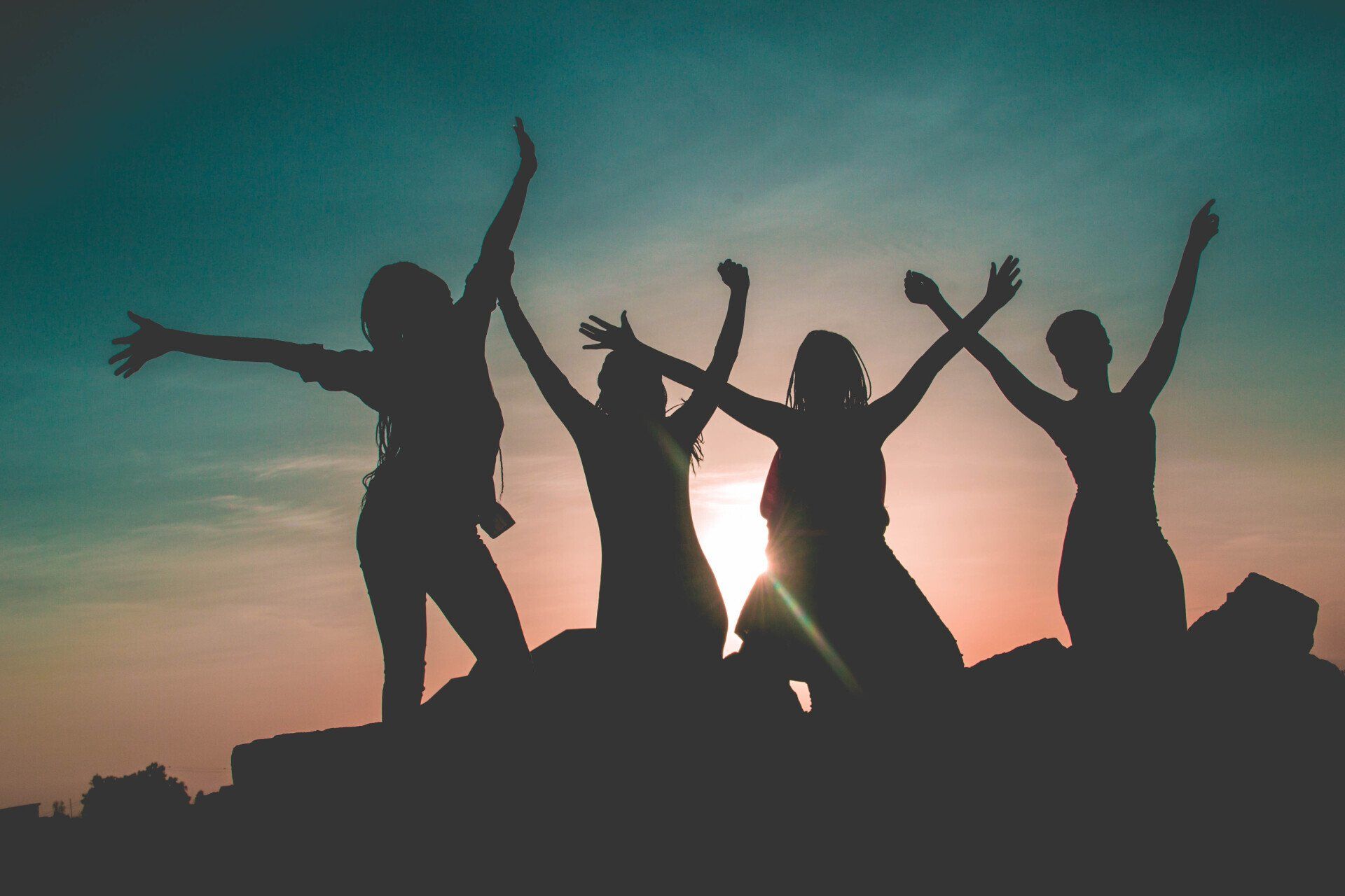 A group of women are sitting on top of a rock with their arms in the air.