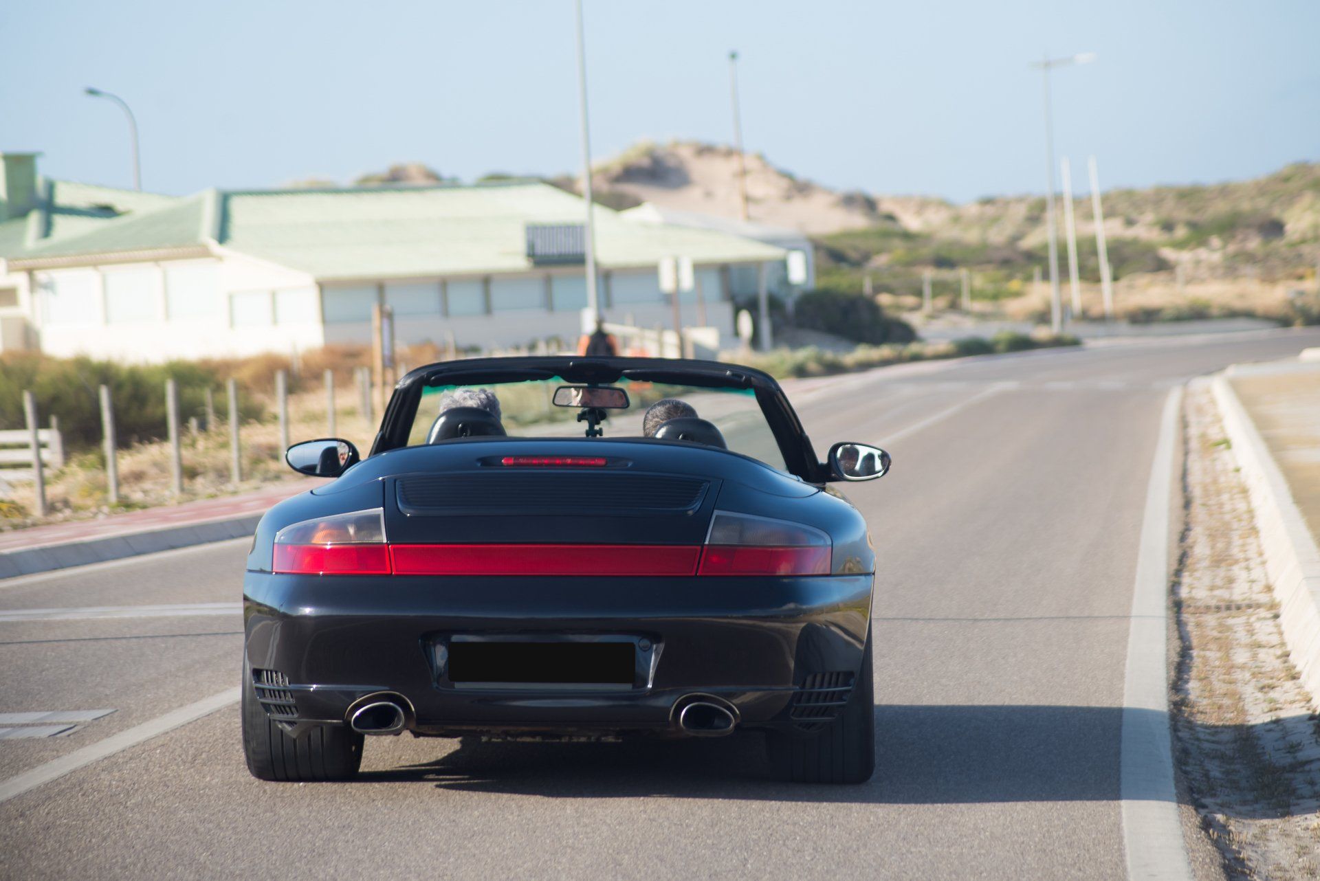 Black convertible car driving on a road near buildings and the coast.