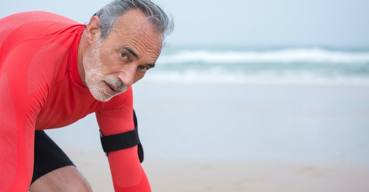 Hombre con camisa roja en la playa, en posición inicial, mirando fijamente a la cámara. El océano al fondo.