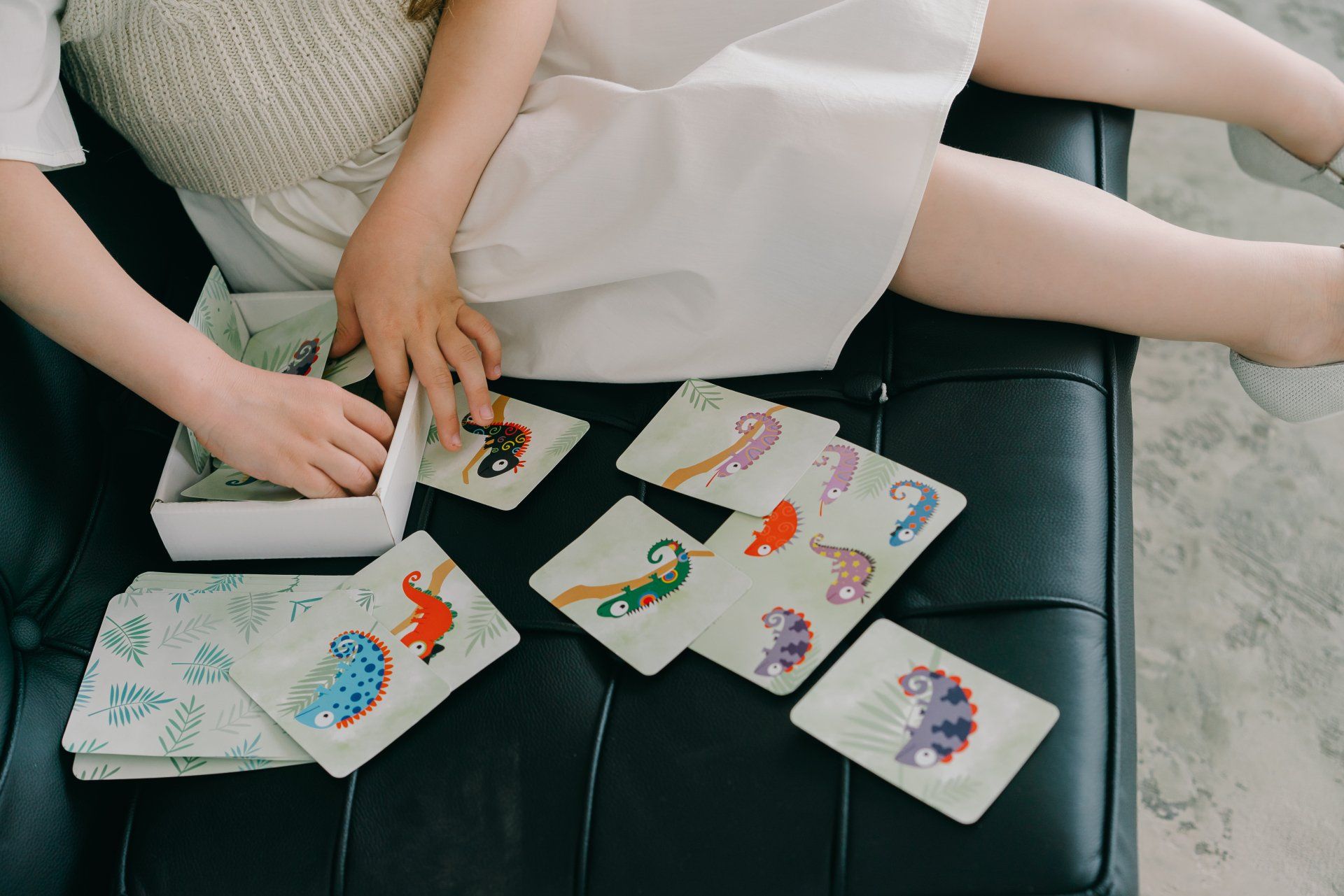 Two people sitting on a couch playing cards with colorful illustrations spread on a table.