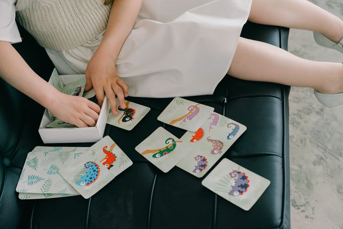 Two people sitting on a couch playing cards with colorful illustrations spread on a table.