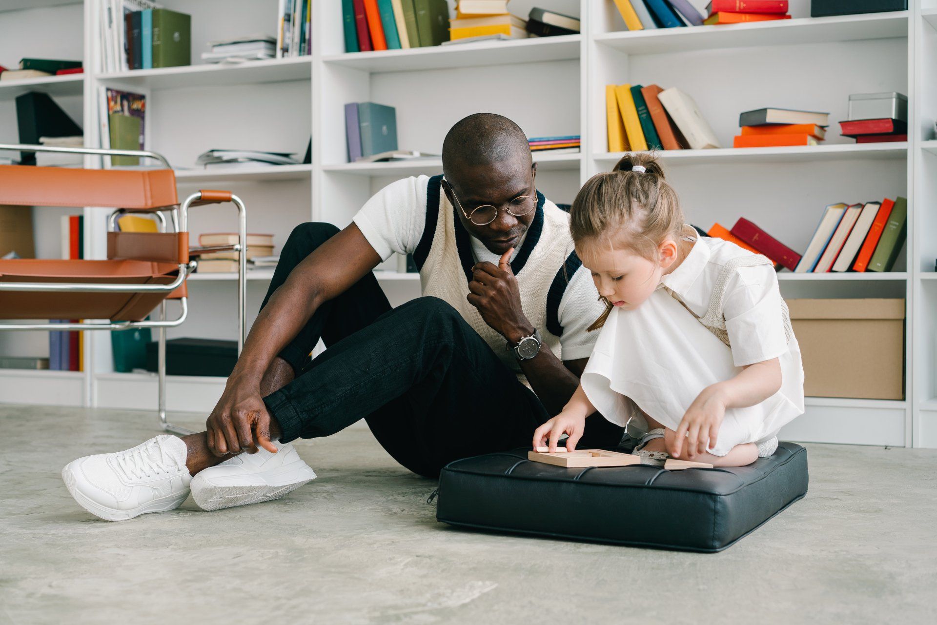 Man and child on floor, looking at a book. Bookshelves in background.