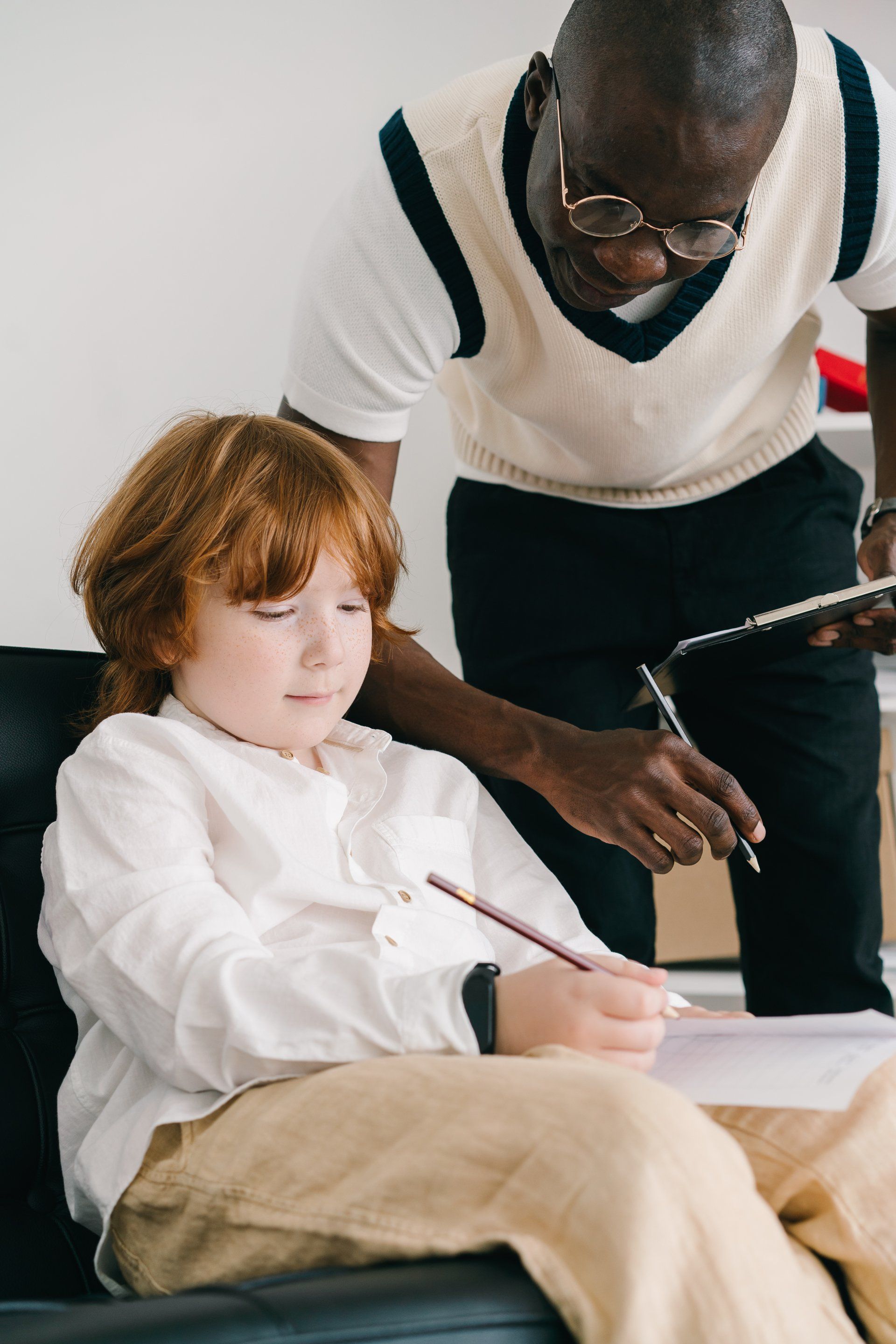 A man is helping a young boy with his homework in a classroom.