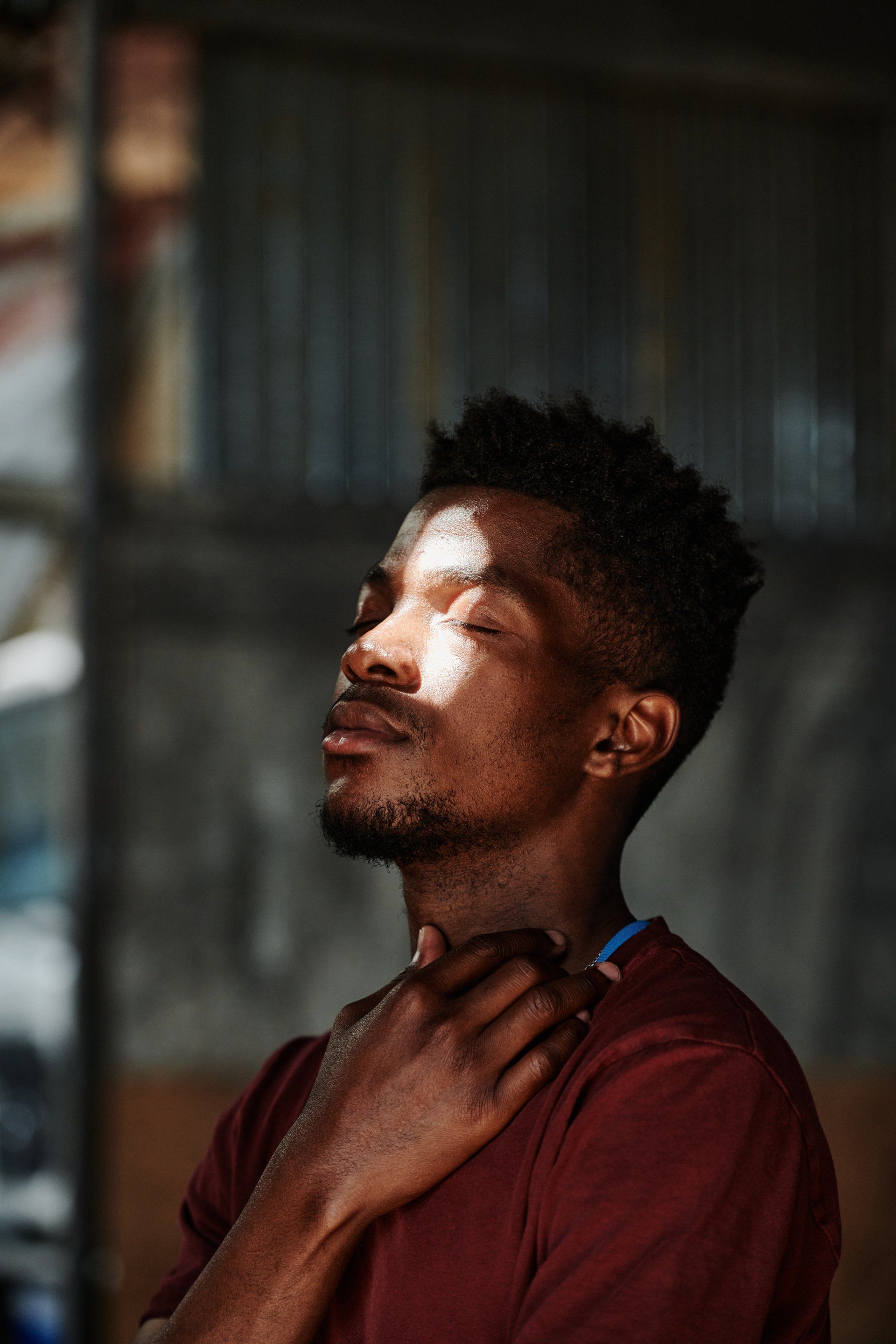 A man is shaving his neck with a razor and the sun is shining on his face.