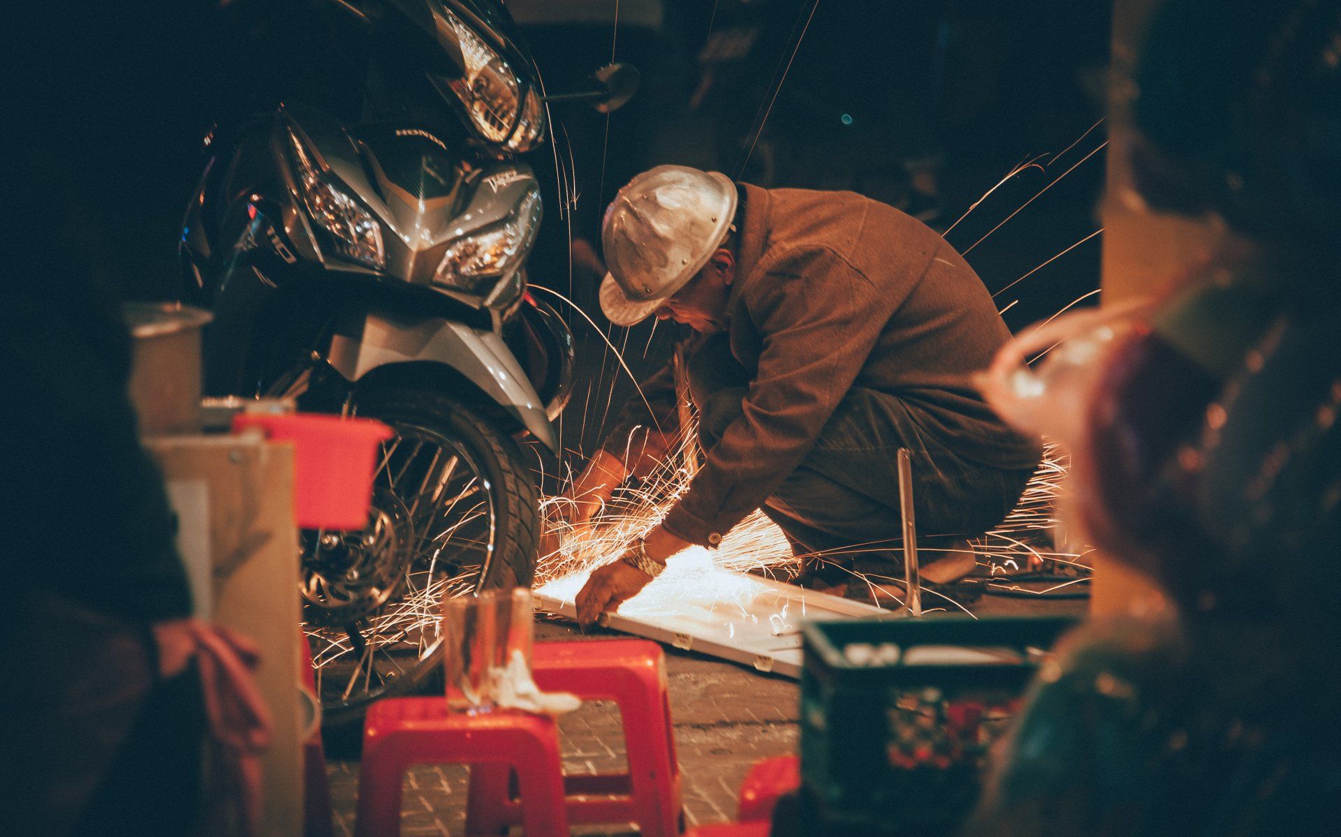 A man is working on a piece of metal next to a motorcycle.