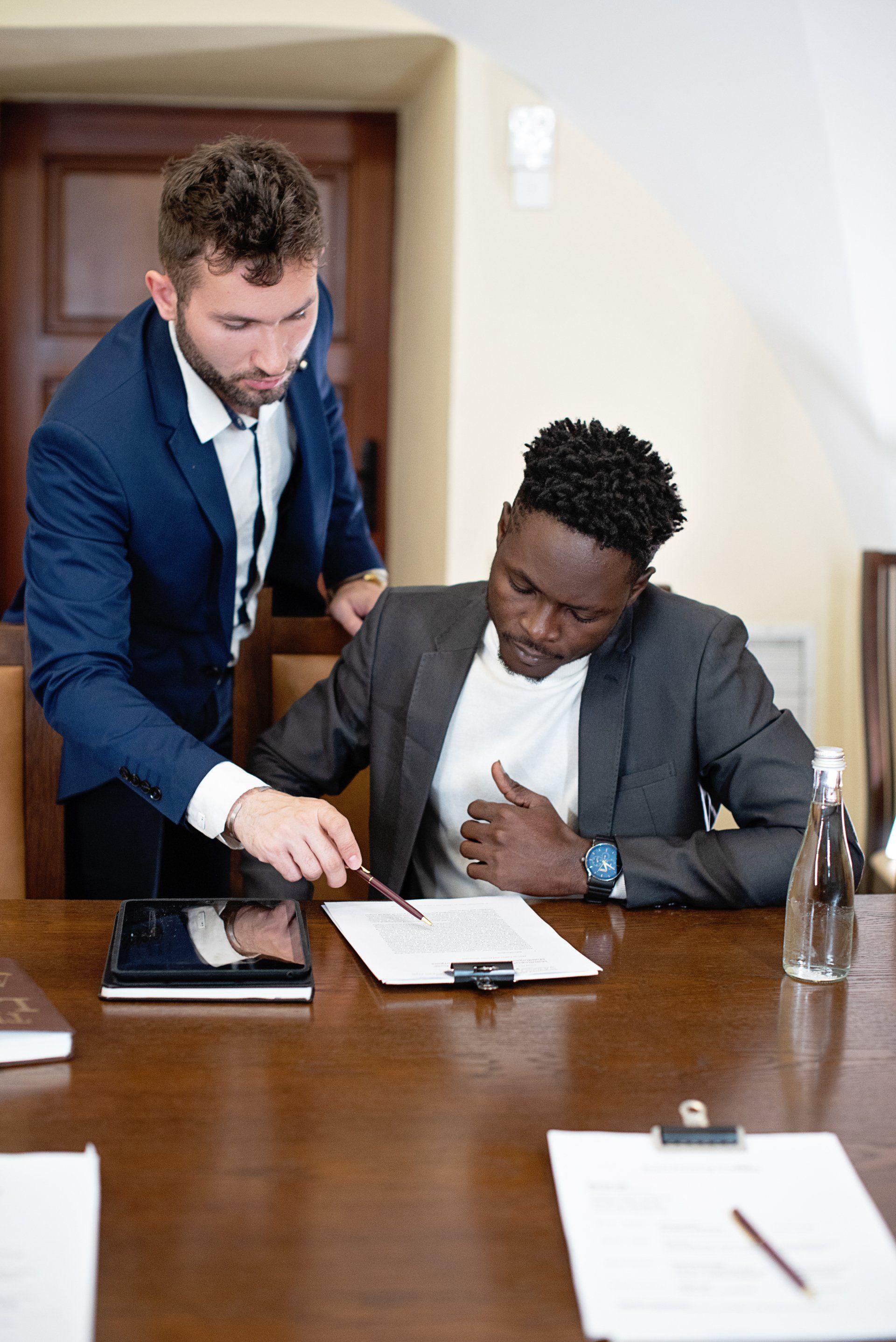Two men are sitting at a table looking at a tablet.