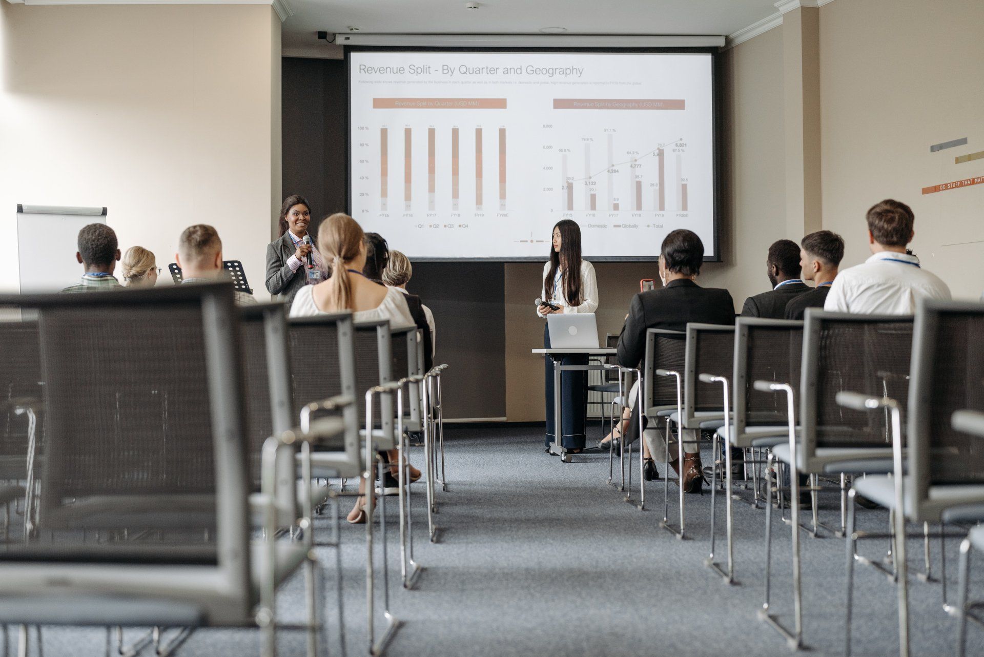 Público sentado em uma sala de conferências assistindo a uma apresentação em uma tela projetada.