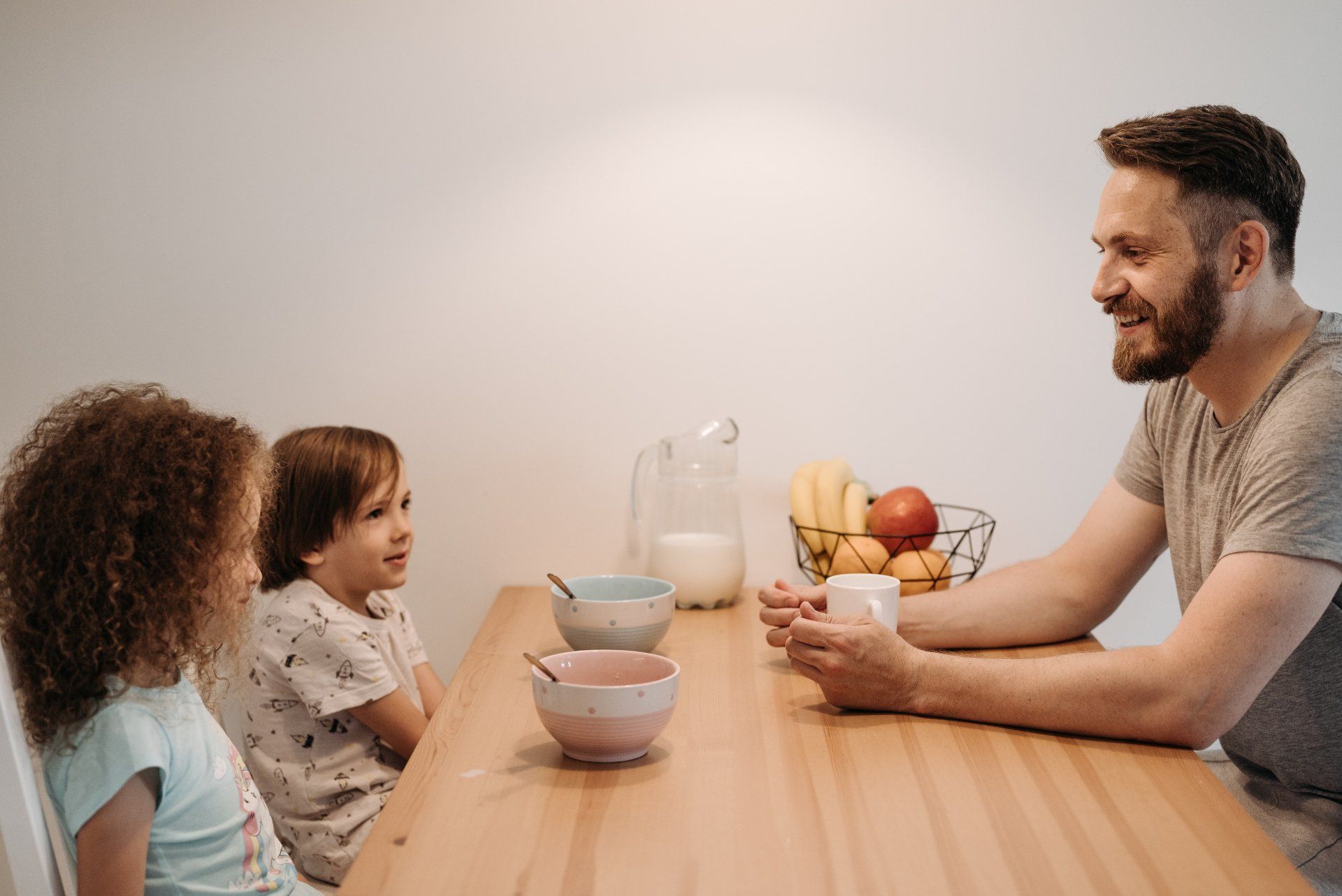 A dad sitting at he breakfast table laughing and smiling while talking to his two kids