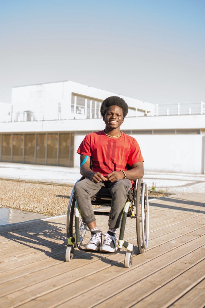 A young man is sitting in a wheelchair on a wooden deck.