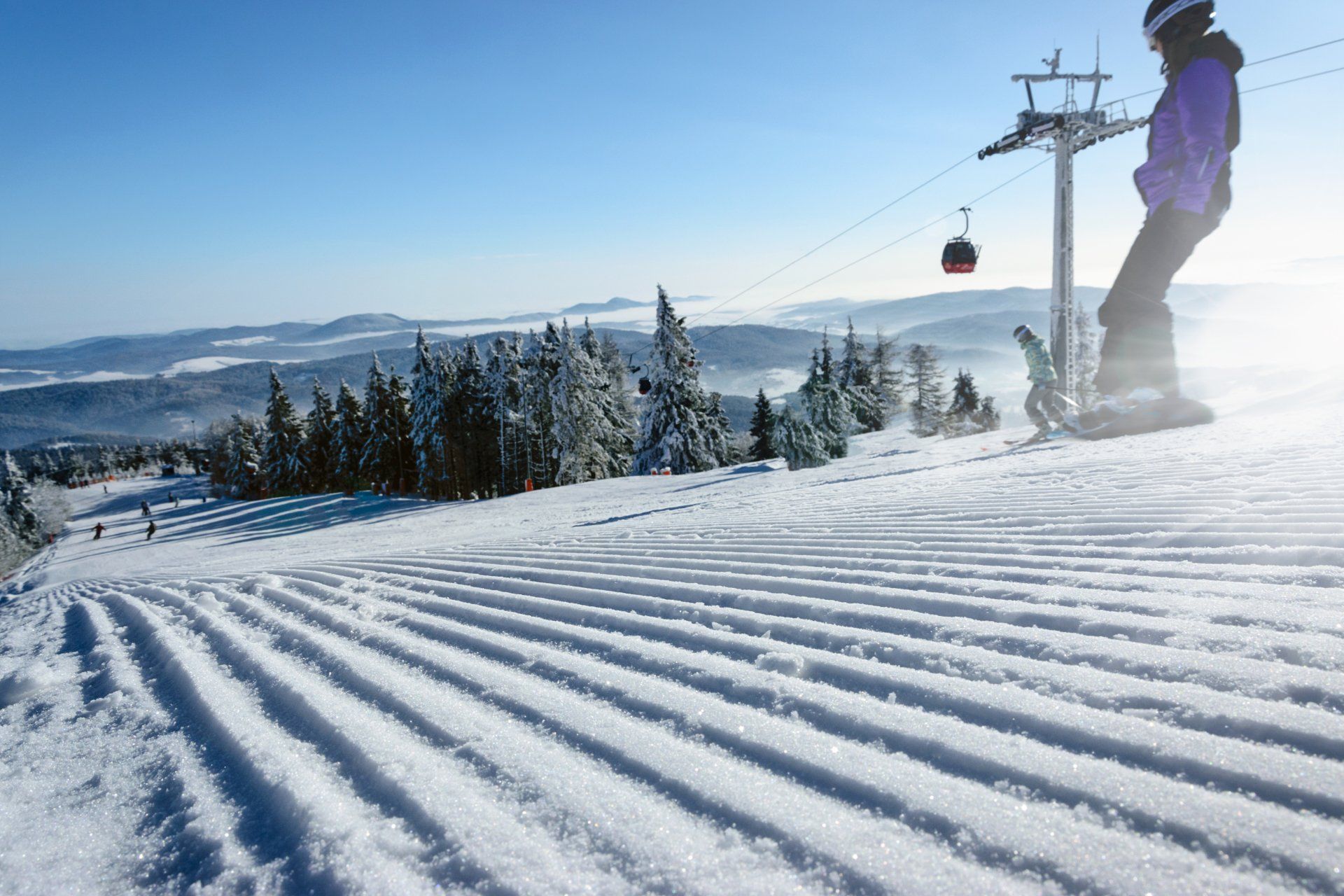 Eine Person fährt einen schneebedeckten Hang hinunter, im Hintergrund ist ein Skilift zu sehen