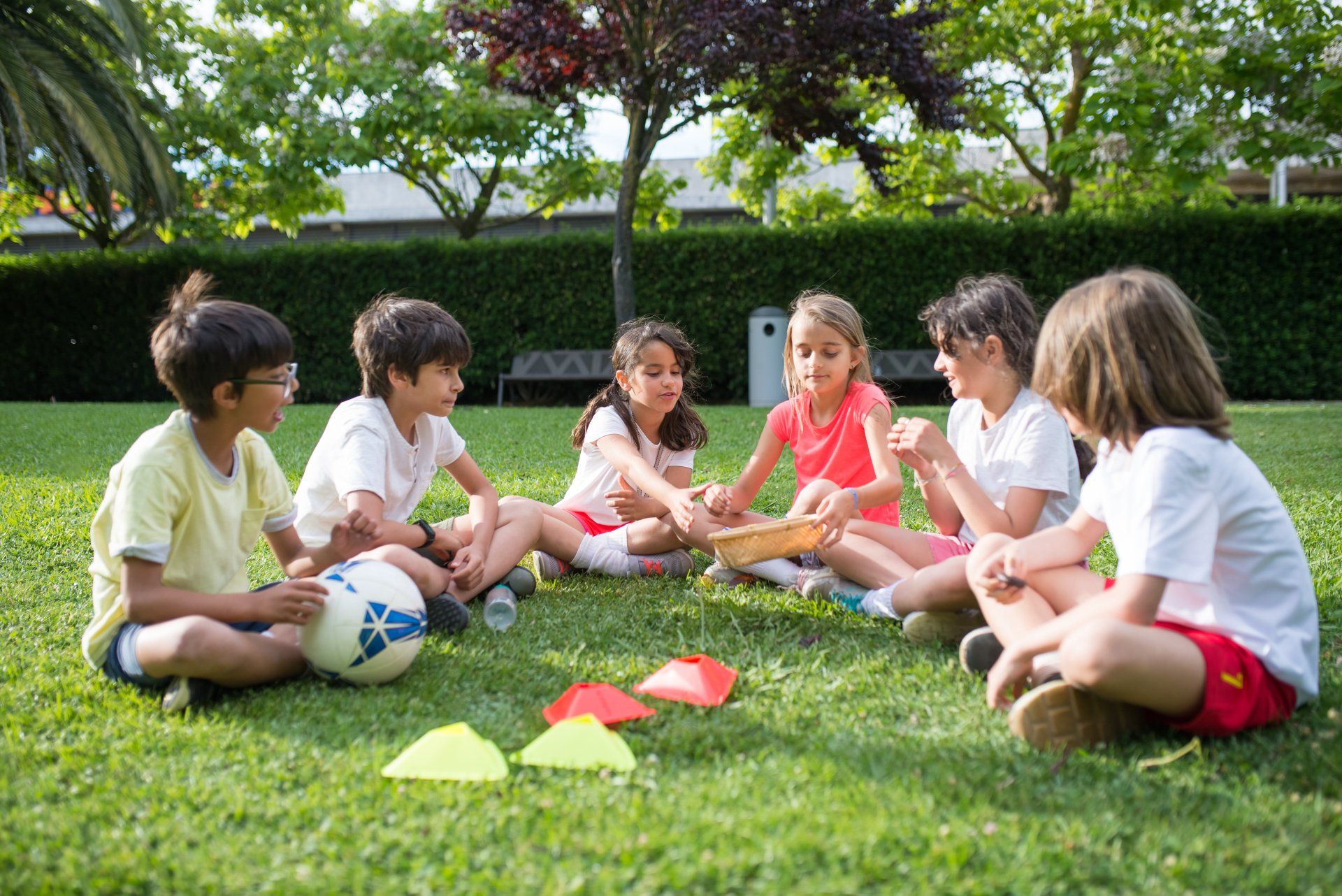 A group of children are sitting in a circle on the grass with a soccer ball.