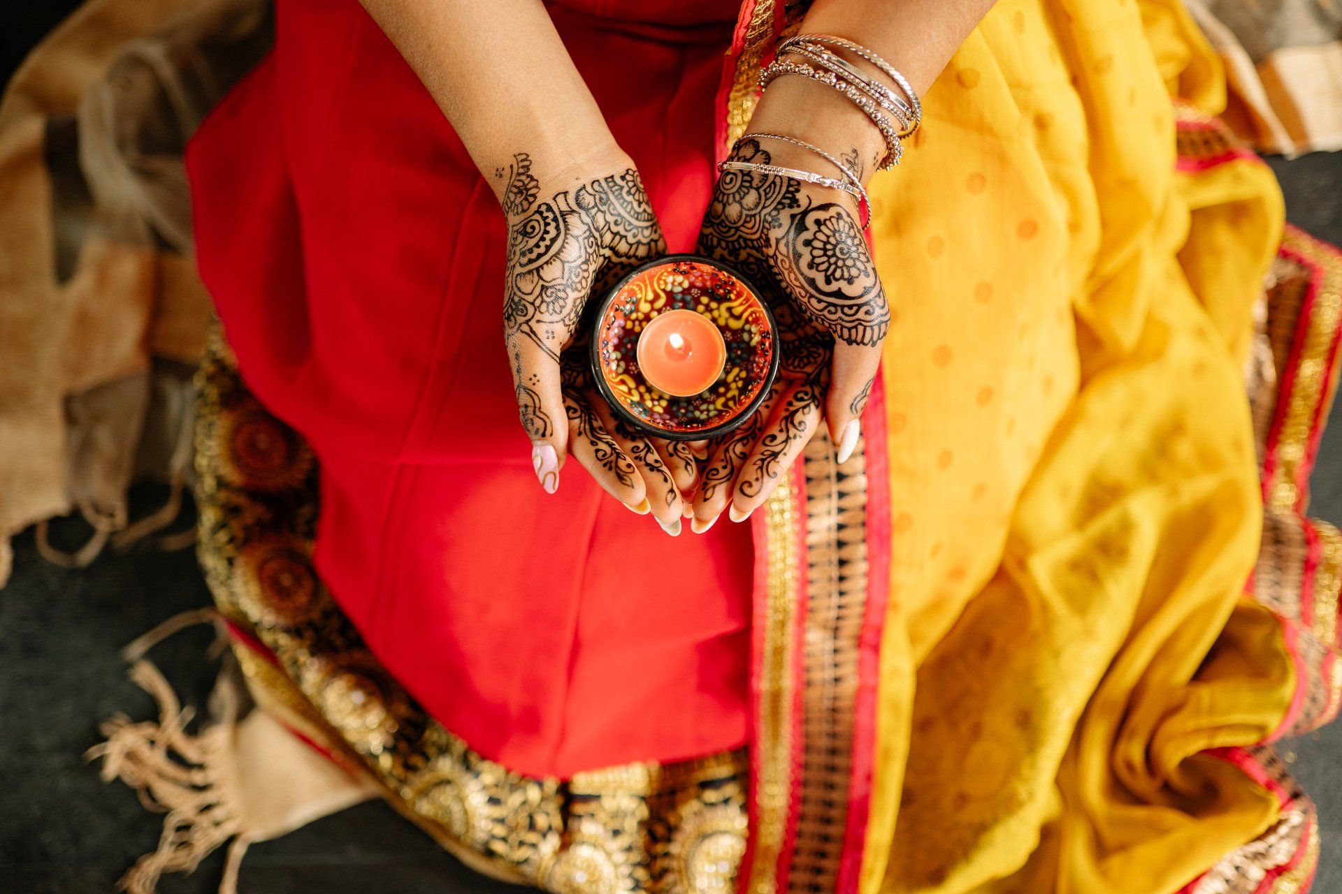 A woman with henna on her hands is holding a candle in her hands.
