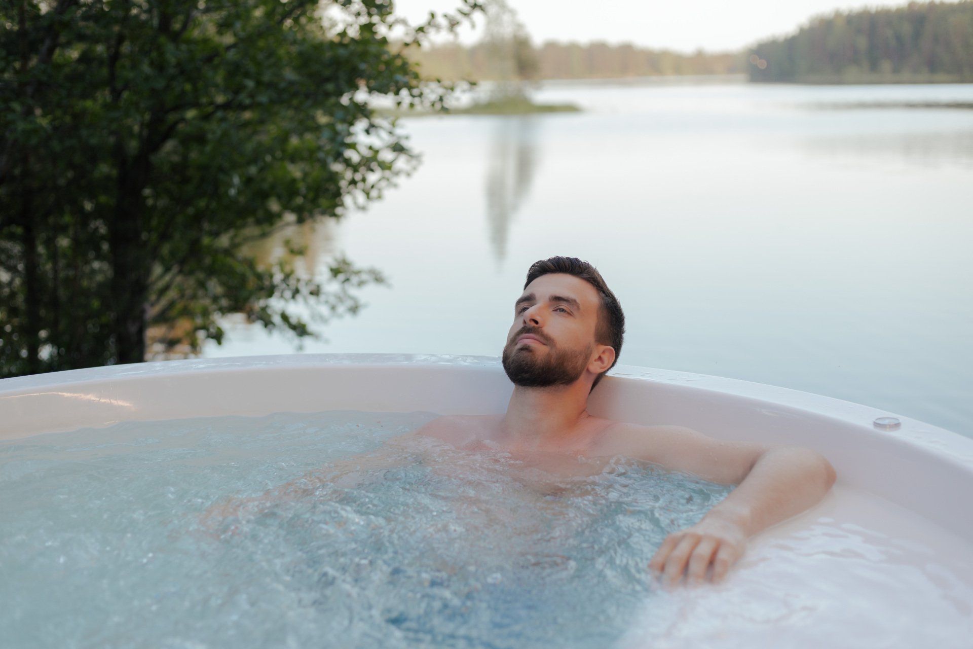 Un homme prend un bain dans un jacuzzi à côté d'un lac.