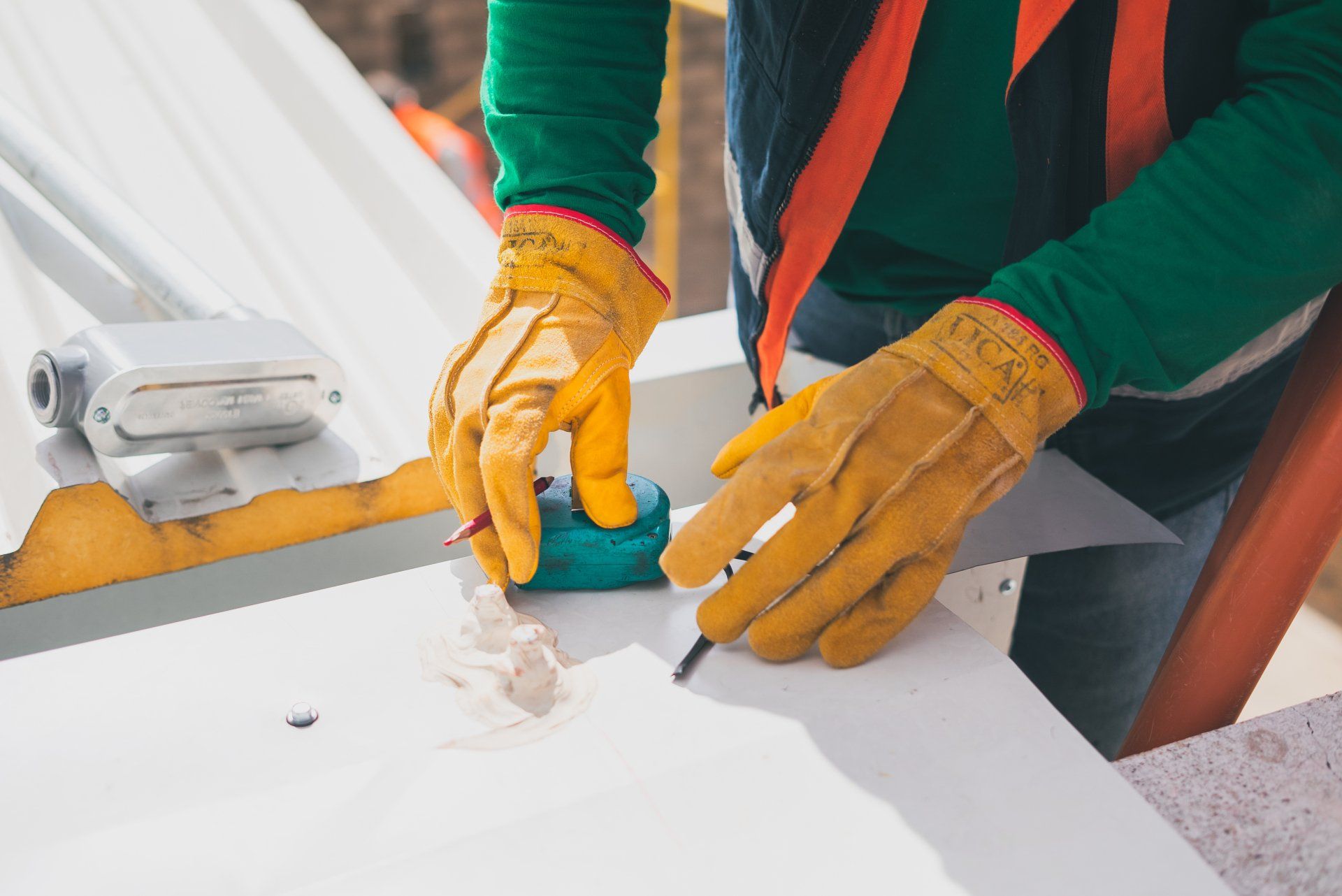 A man wearing yellow gloves is measuring a piece of metal with a tape measure.