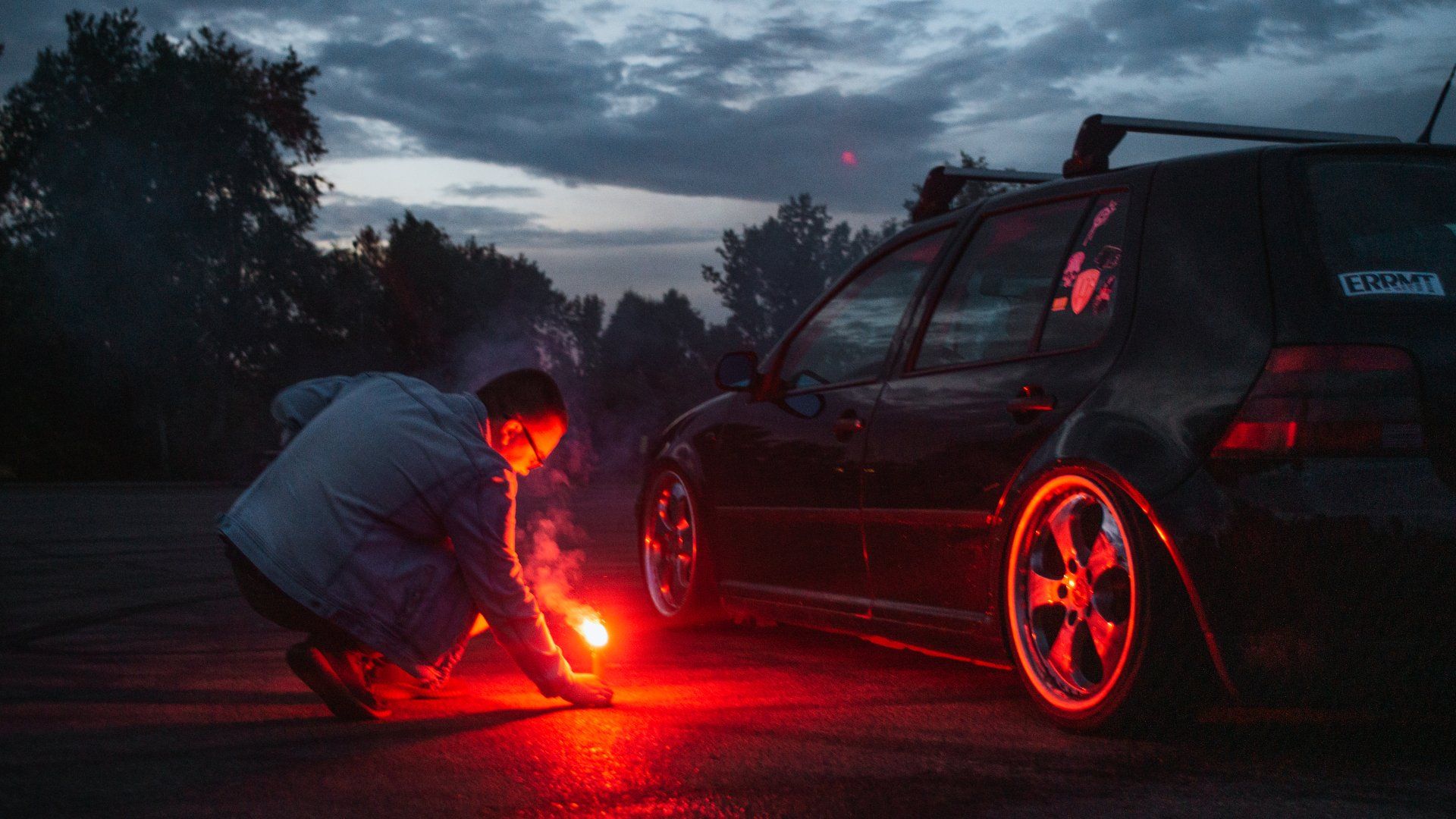 A man is kneeling down next to a car with a red light on it.