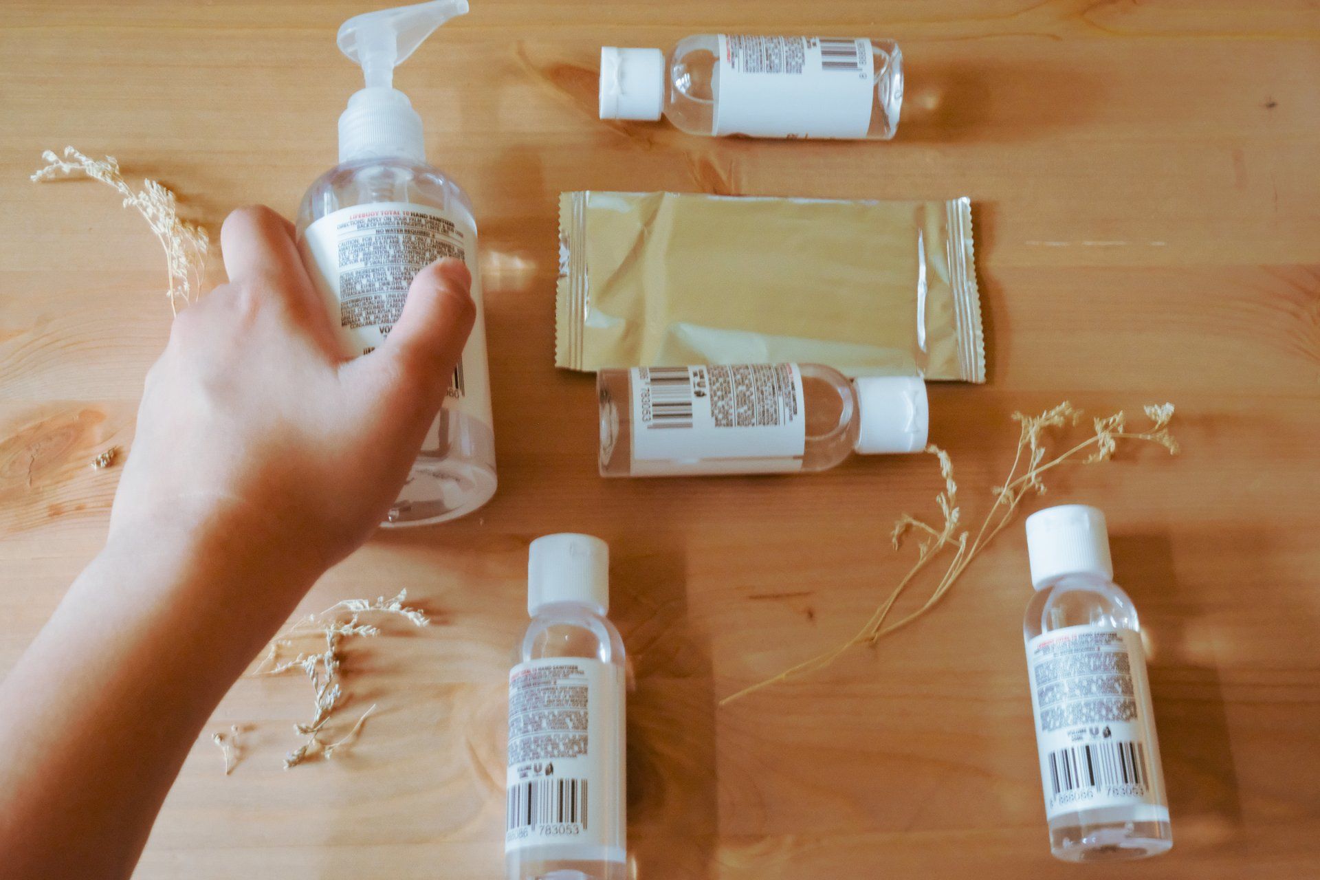 A person is reaching for a bottle of hand sanitizer on a wooden table.