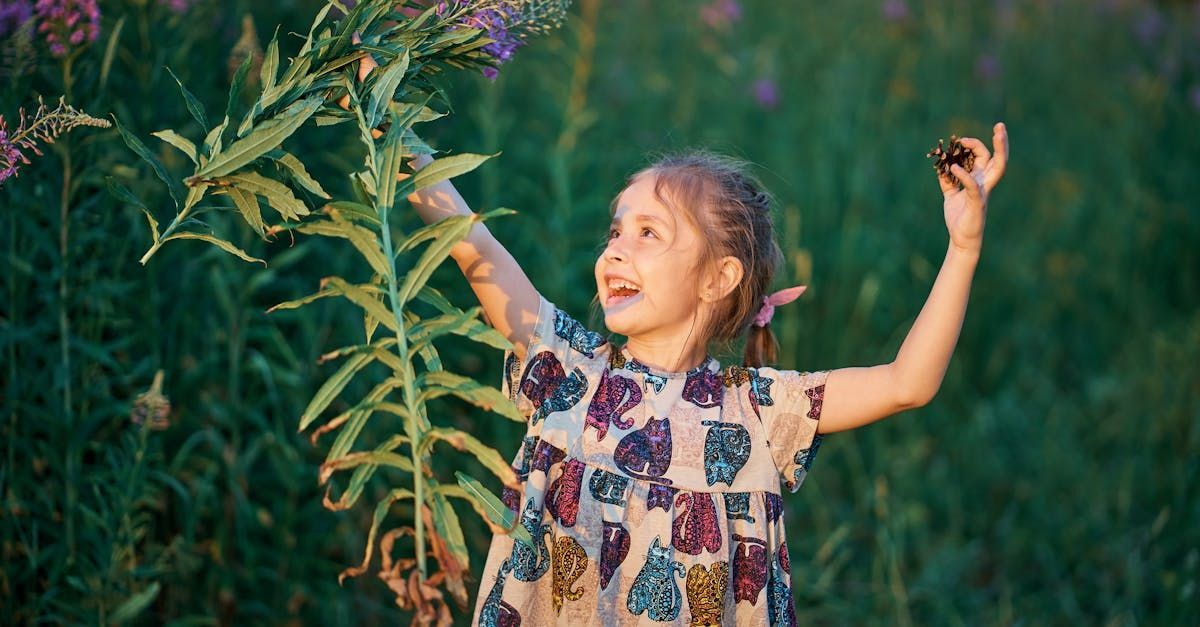 A little girl is holding a plant in her hands in a field.