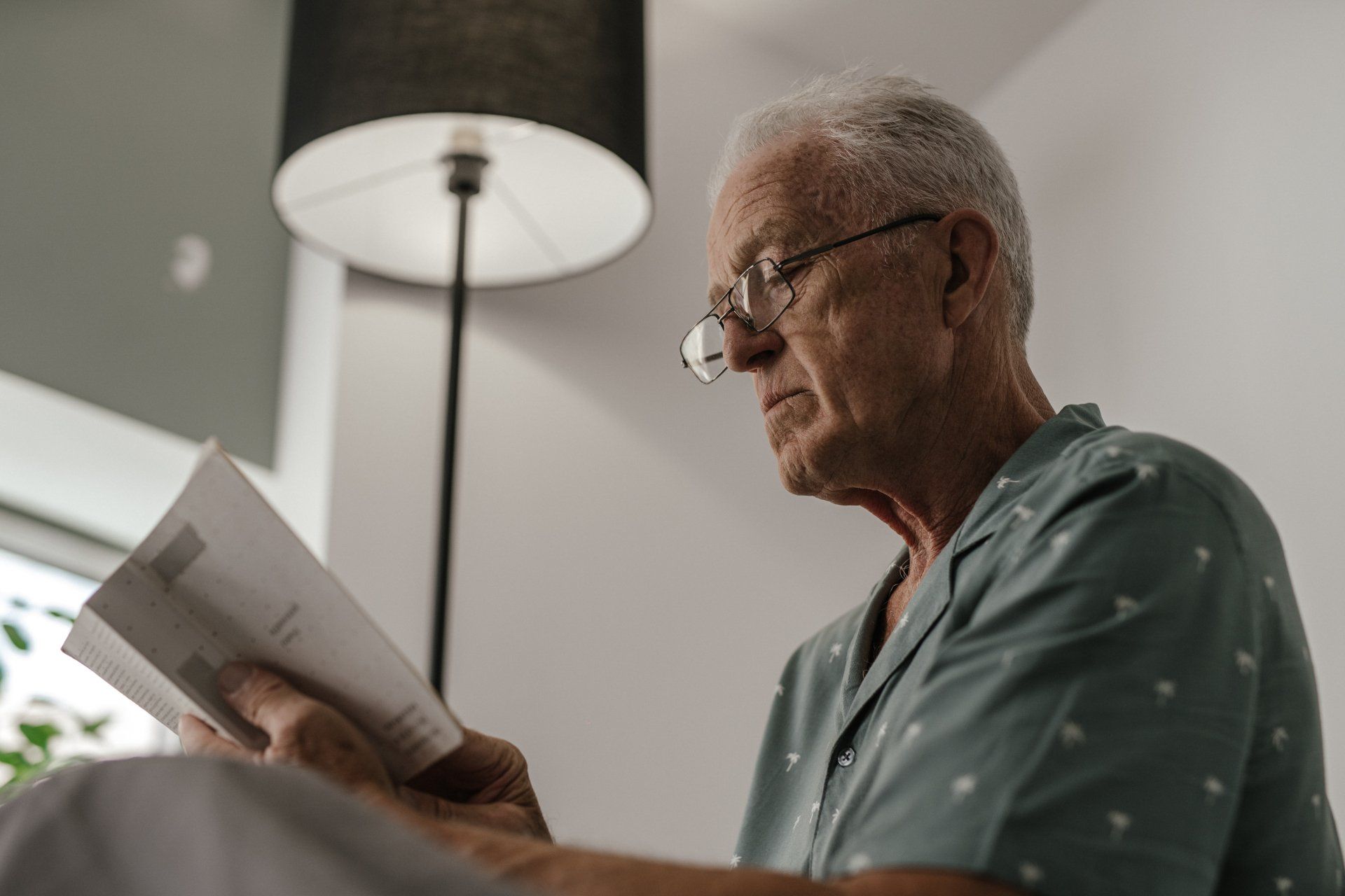 An elderly man wearing glasses is reading a piece of paper.