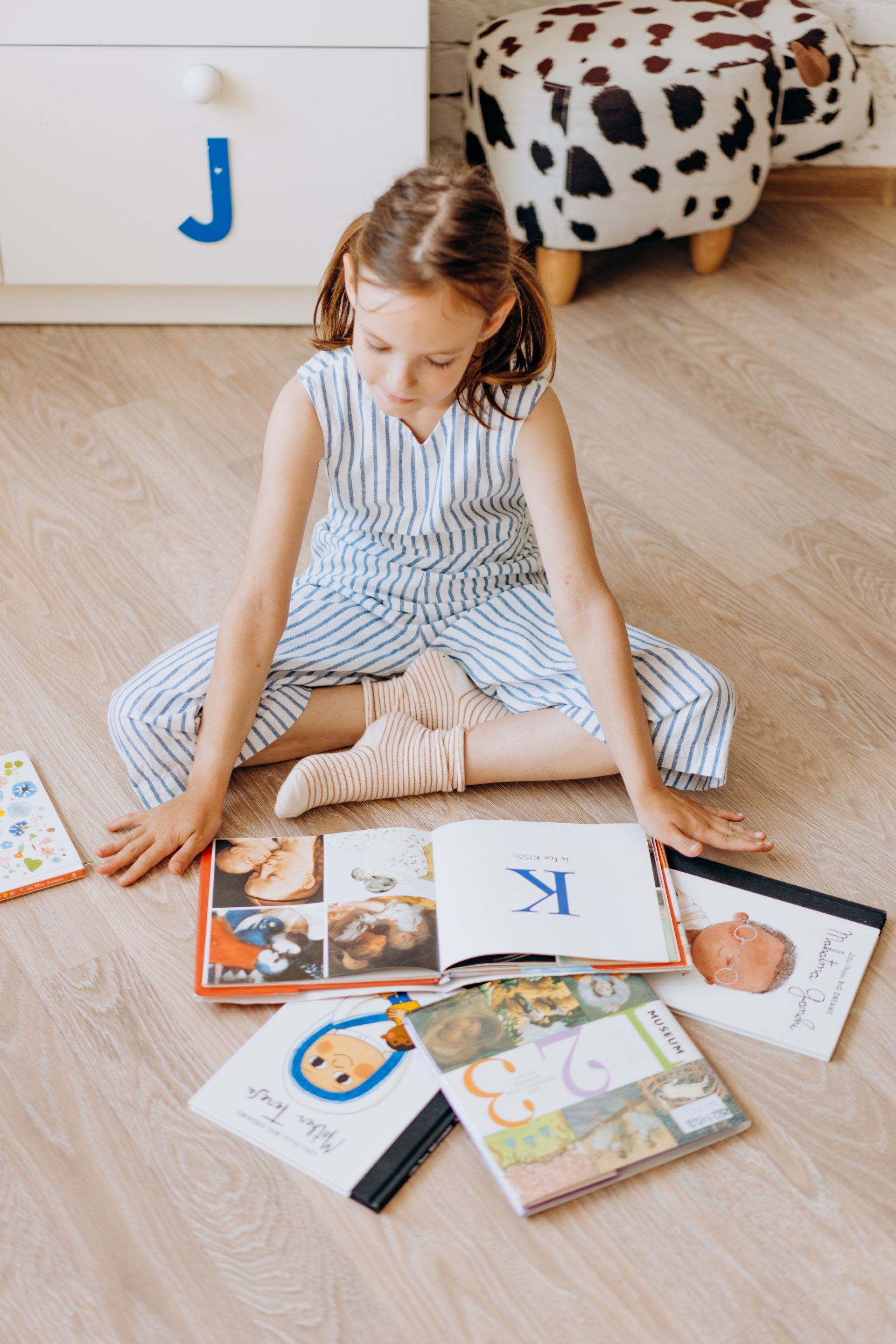 Child sitting on the floor reading colorful picture books in a bright room
