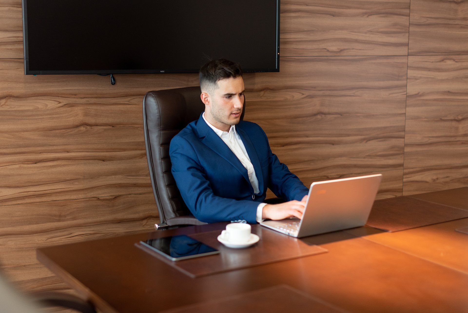 A man in a suit is sitting at a table using a laptop computer.