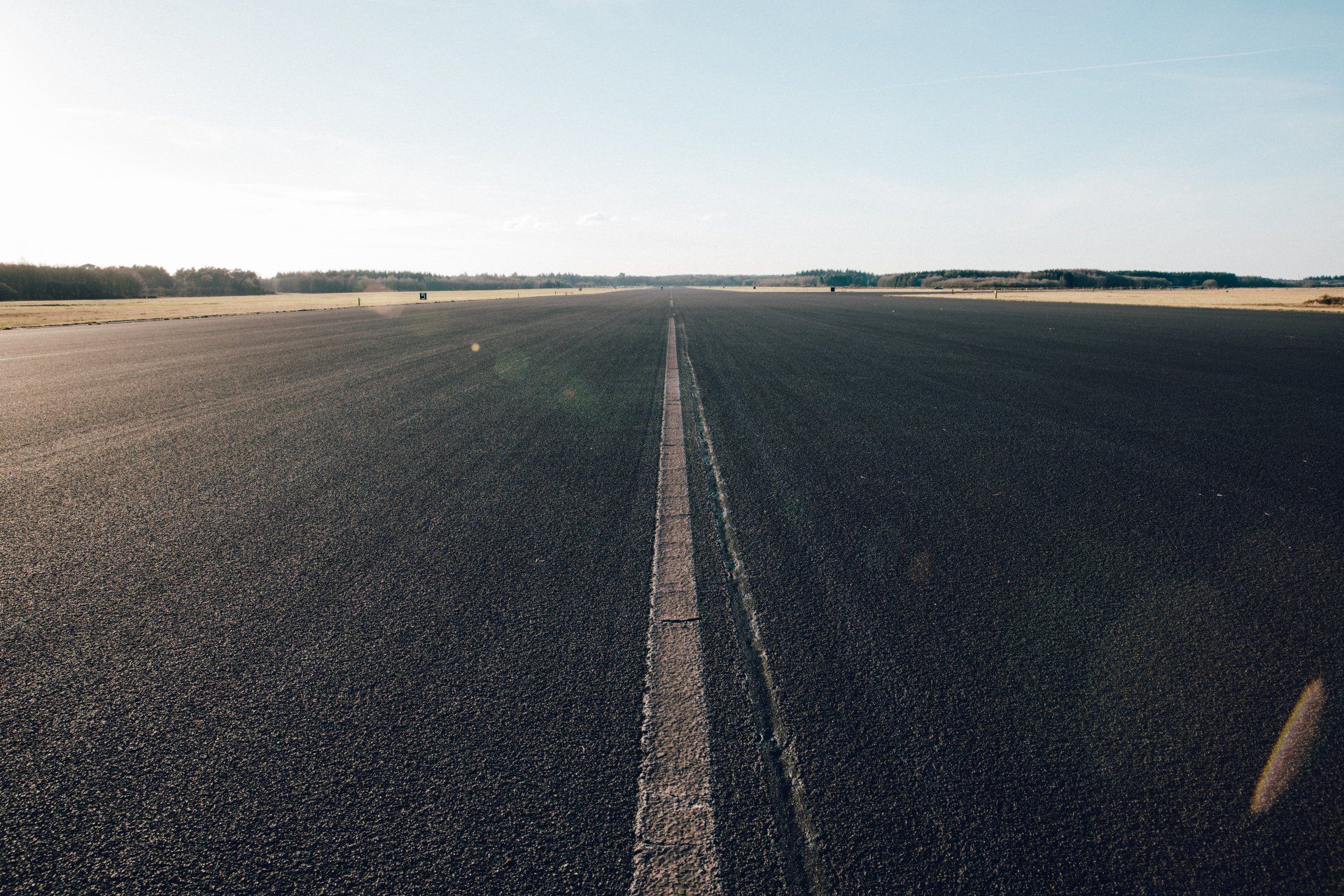 Empty asphalt road stretching into a flat horizon under a pale sky.