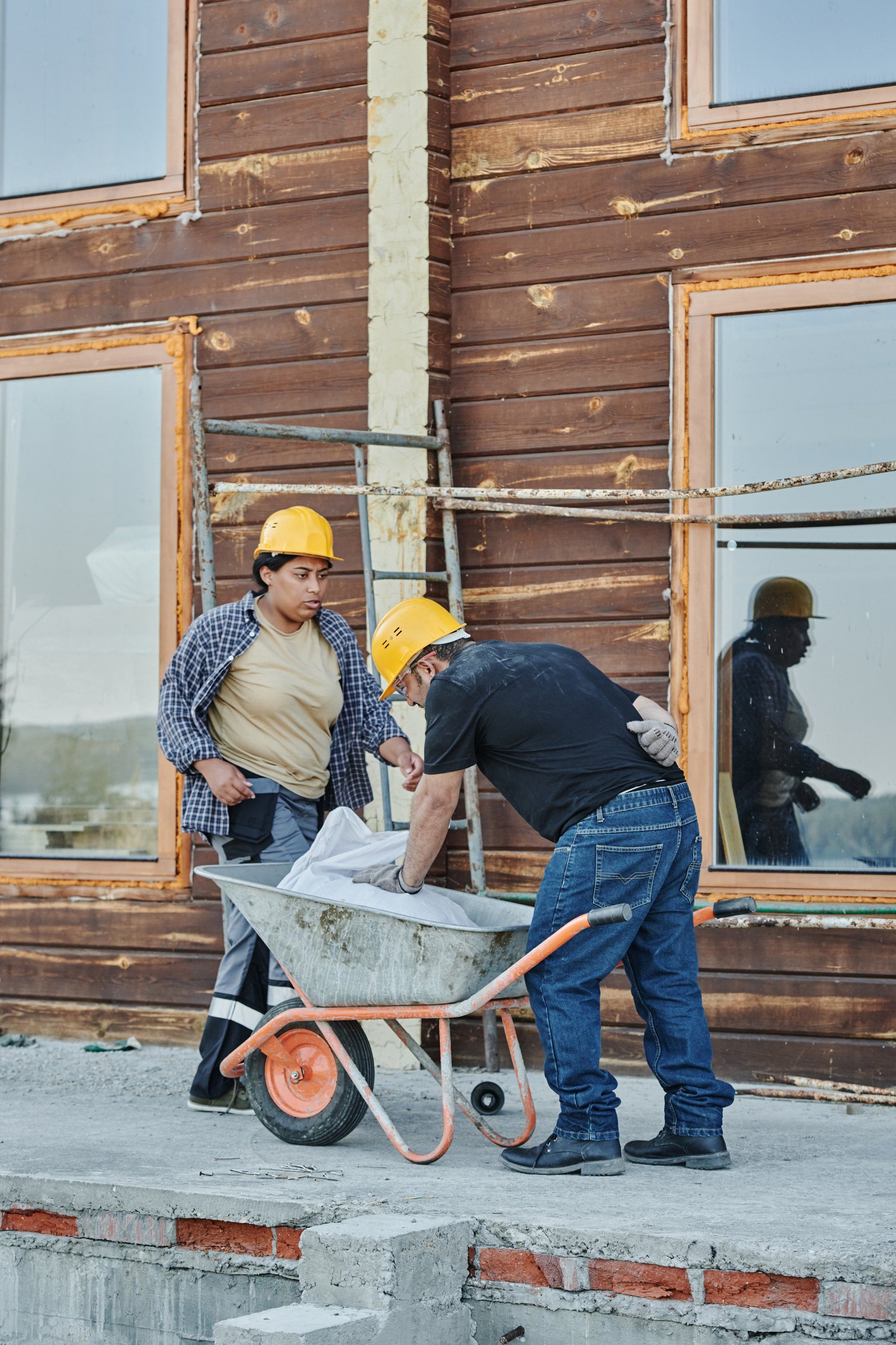 A man is pushing a wheelbarrow while a woman looks on.