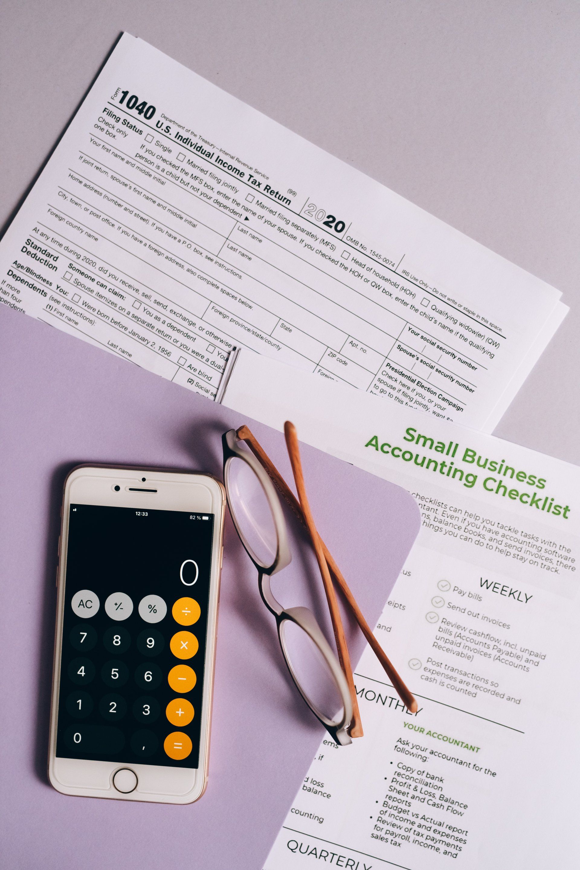 A cell phone calculator glasses and a small business accounting checklist are on a table.