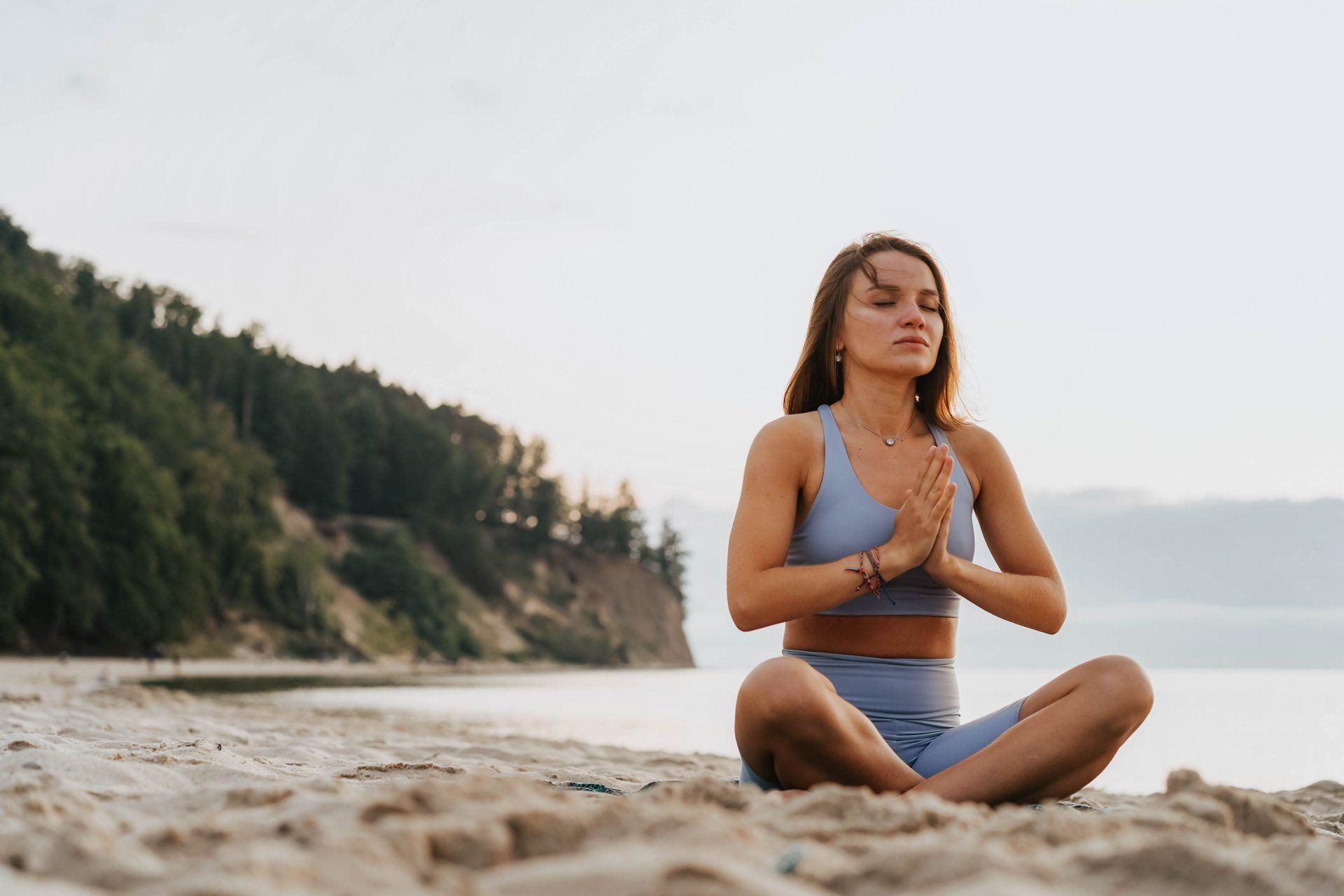 Une femme est assise en position du lotus sur la plage.